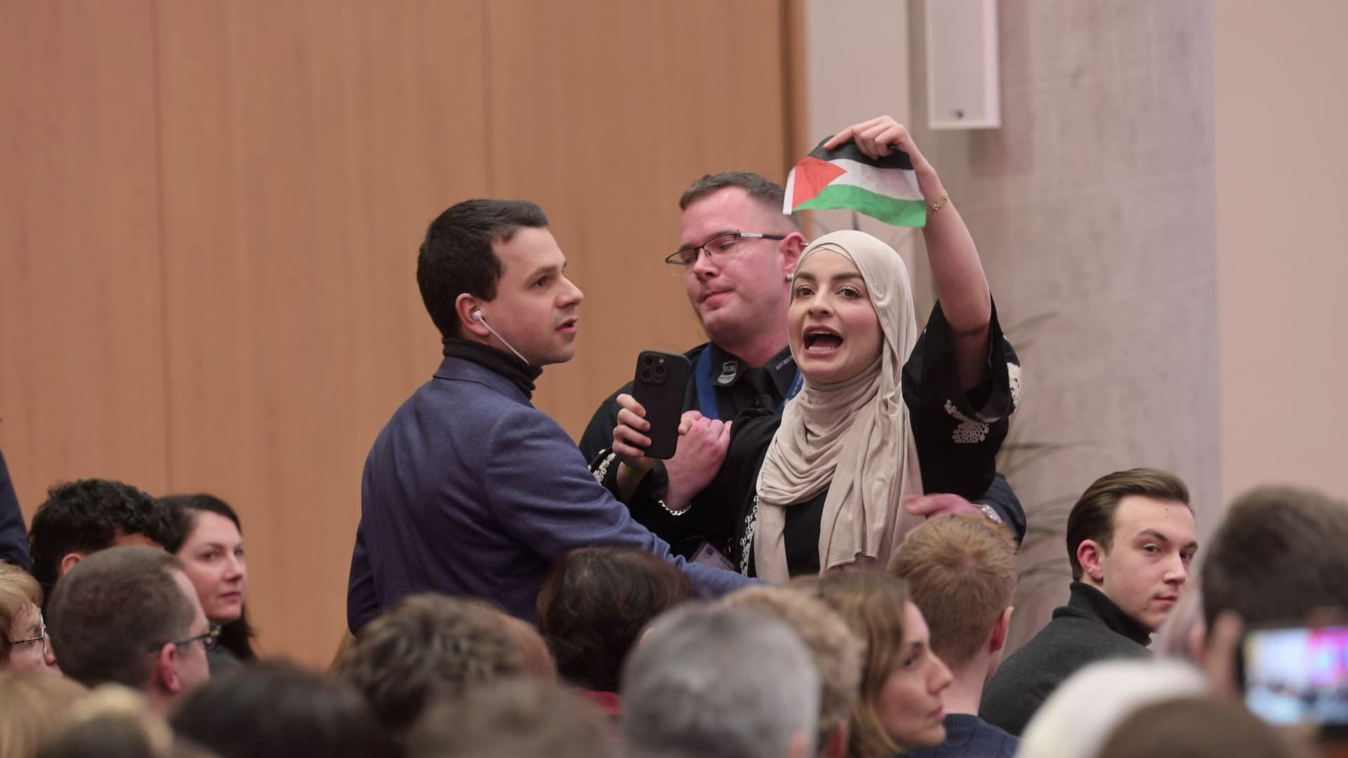 Eine pro-palästinensische Fragestellerin wird bei einem Bürgerdialog mit Bundeskanzler Scholz aus dem Campus geleitet.