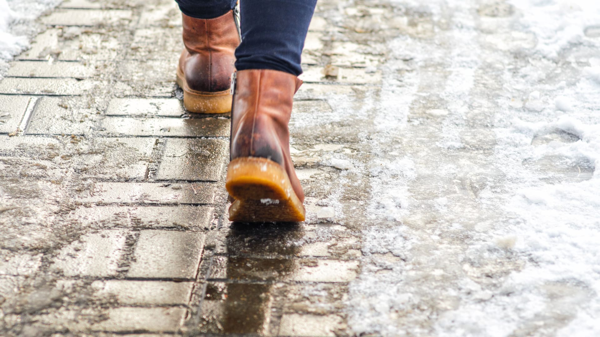 Jemand läuft mit Winterschuhen auf dem Bürgersteig: Kühlen die Zehen aus, weil die Schuhe durchfeuchtet sind, steigt das Risiko für Frostbeulen.