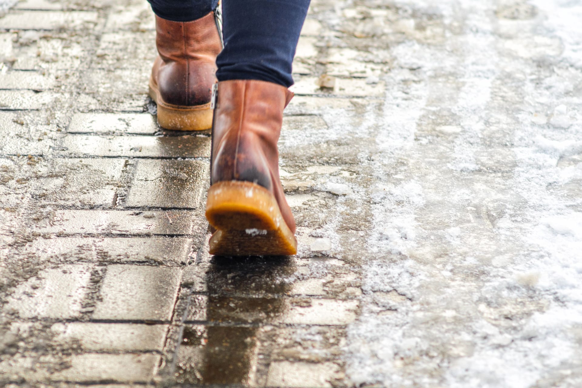 Jemand läuft mit Winterschuhen auf dem Bürgersteig: Kühlen die Zehen aus, weil die Schuhe durchfeuchtet sind, steigt das Risiko für Frostbeulen.