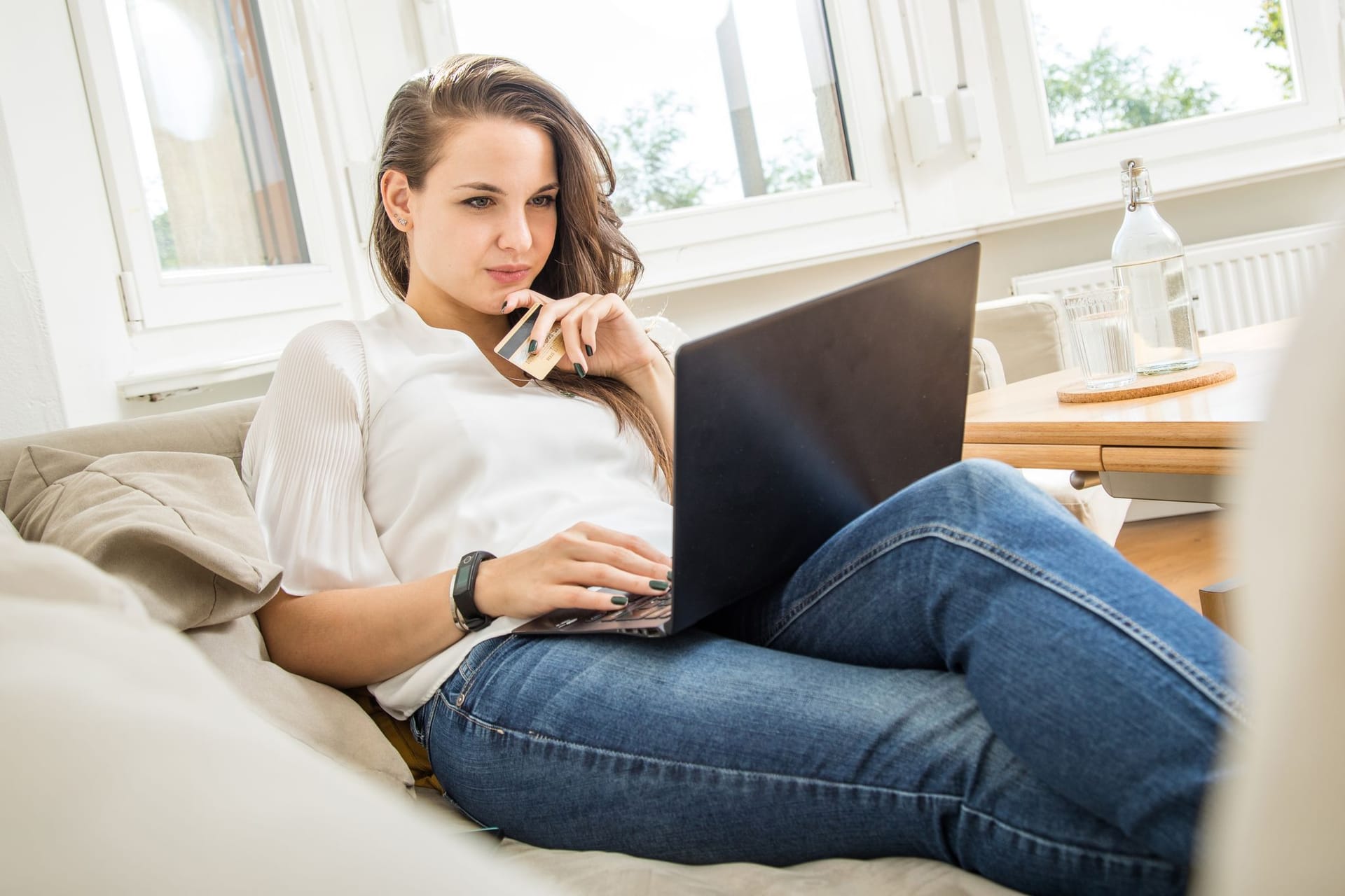 Frau mit Geldkarte in der Hand schaut auf einen Laptop