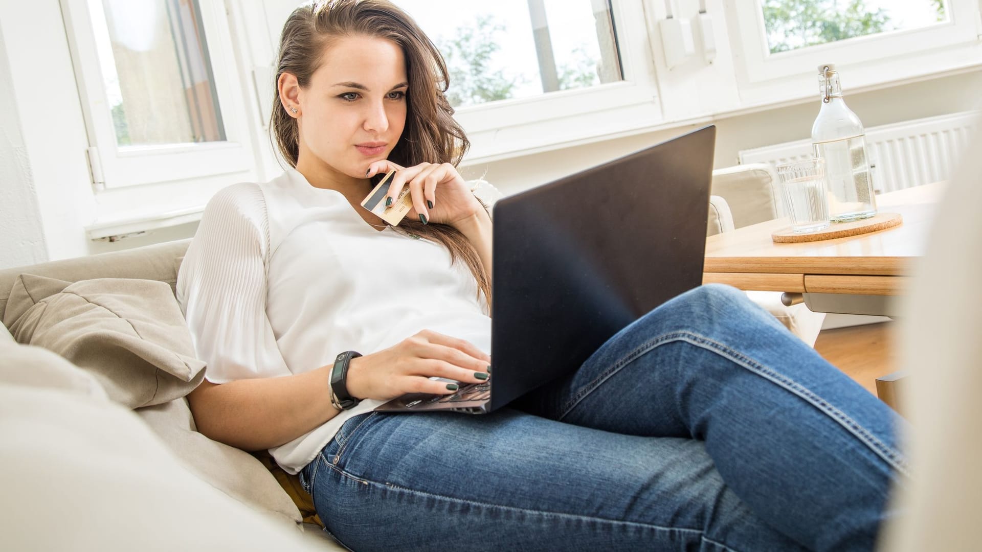 Frau mit Geldkarte in der Hand schaut auf einen Laptop