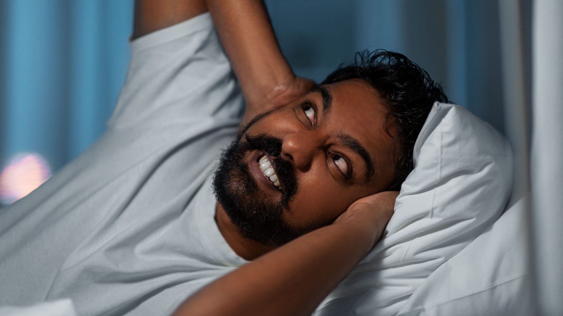 annoyed indian man lying in bed and closing ears