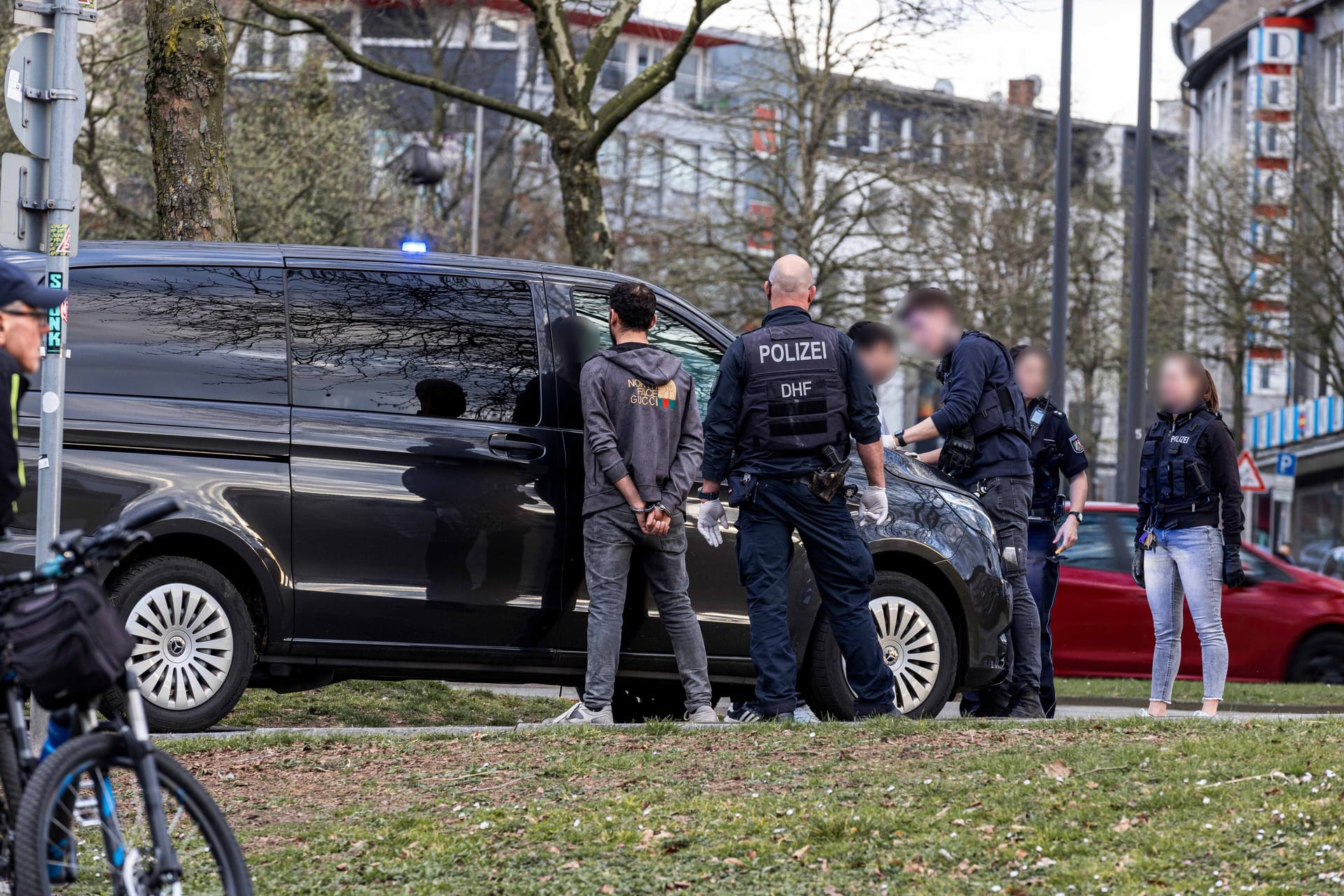 Ein mit Handschellen gefesselter Mann steht vor einem Polizeiauto: Das Opfer soll nicht in Lebensgefahr schweben.