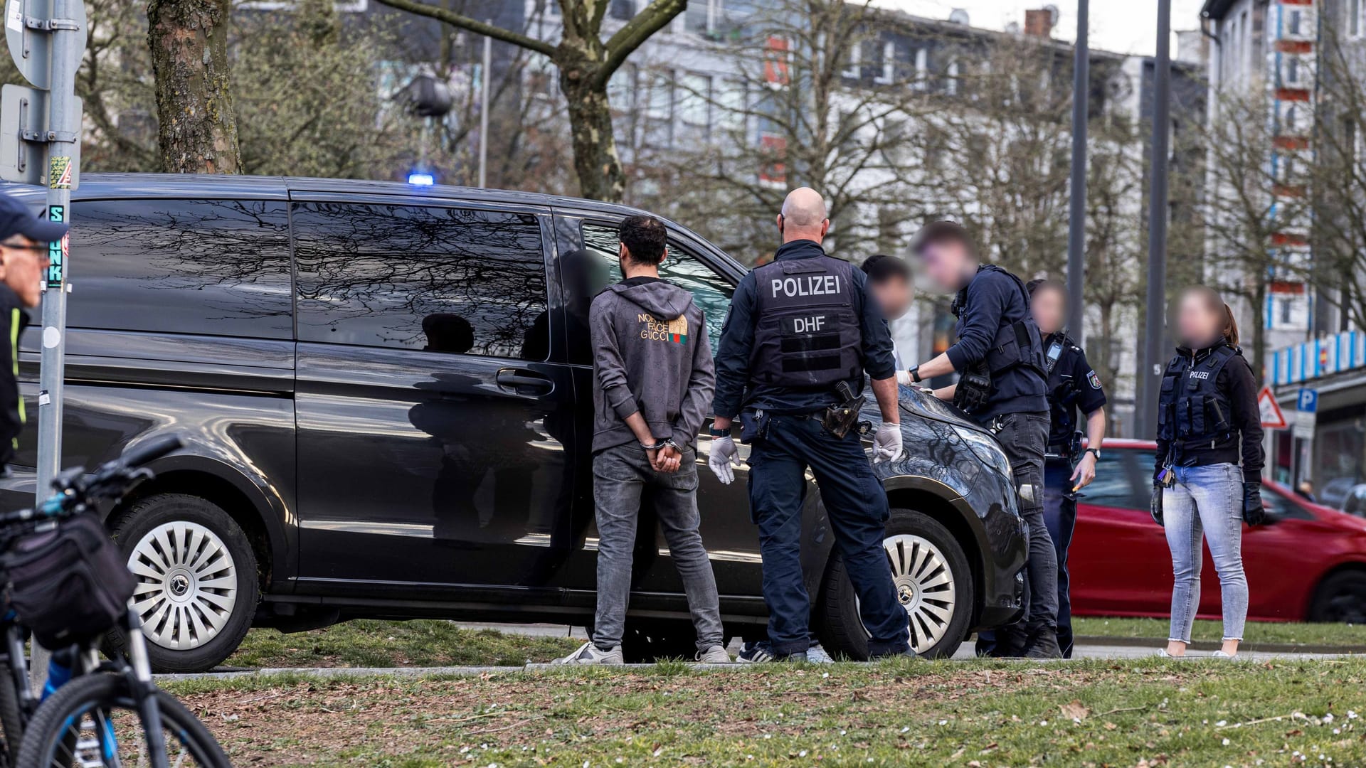 Ein mit Handschellen gefesselter Mann steht vor einem Polizeiauto: Das Opfer soll nicht in Lebensgefahr schweben.