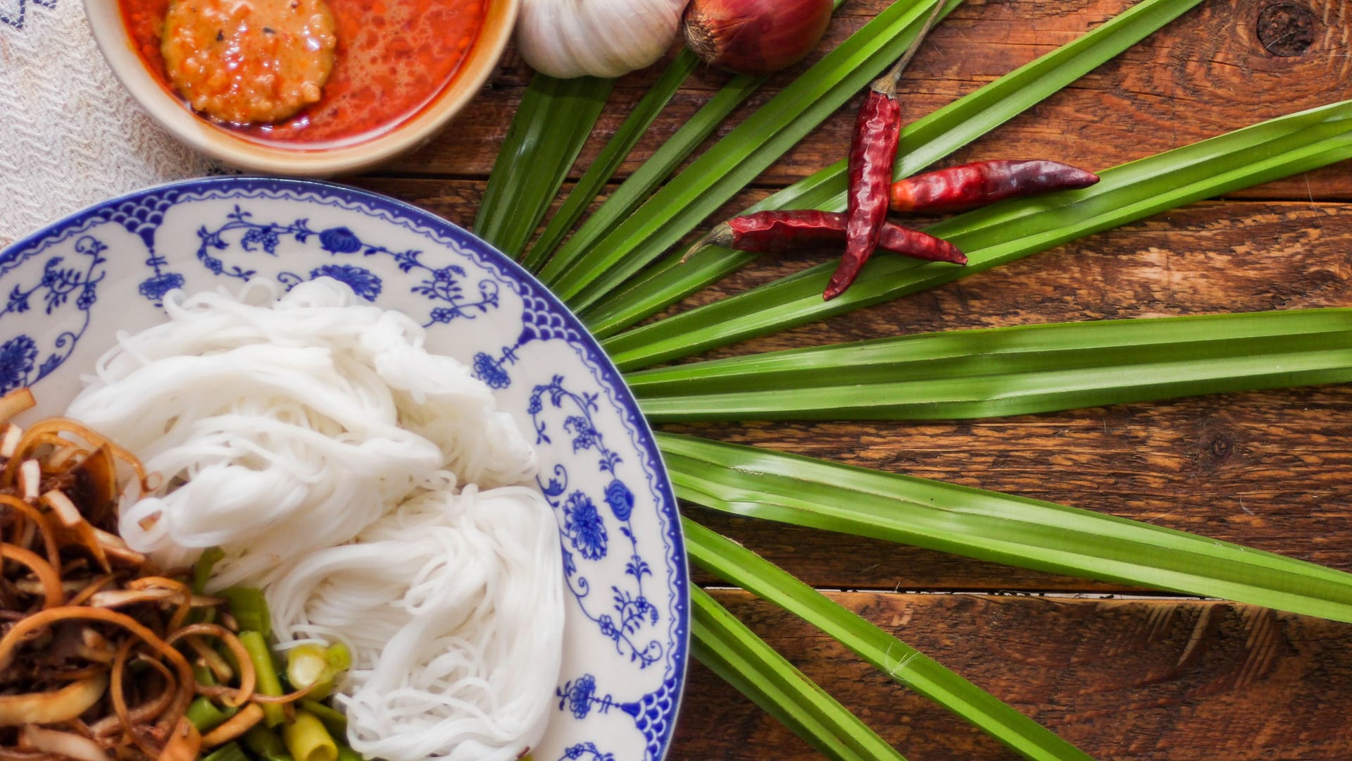 Thai rice noodle with peanut sauce served in a white plate on a wooden table and decorated with leaves.