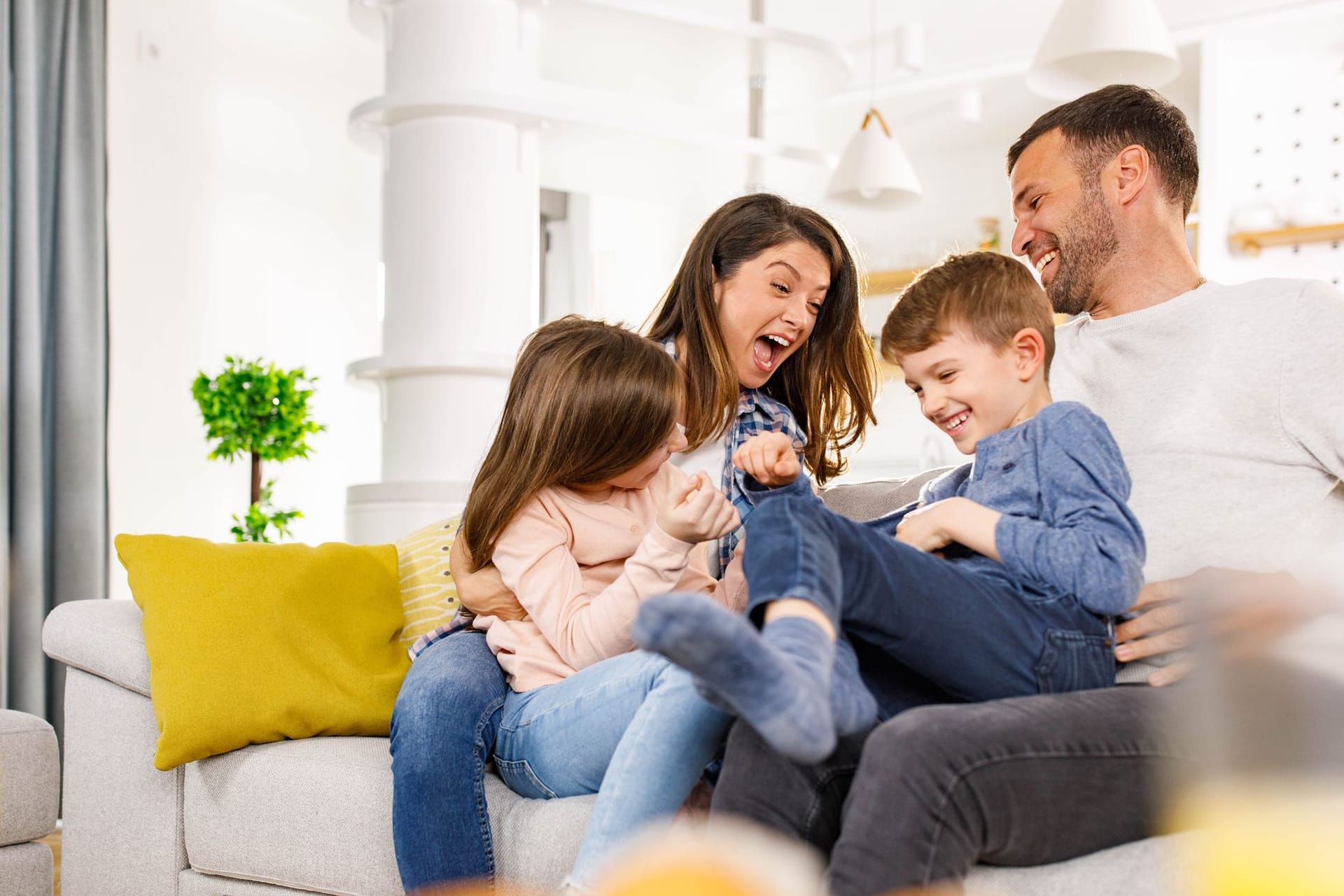 Familie mit zwei Kindern sitzt fröhlich auf dem Sofa