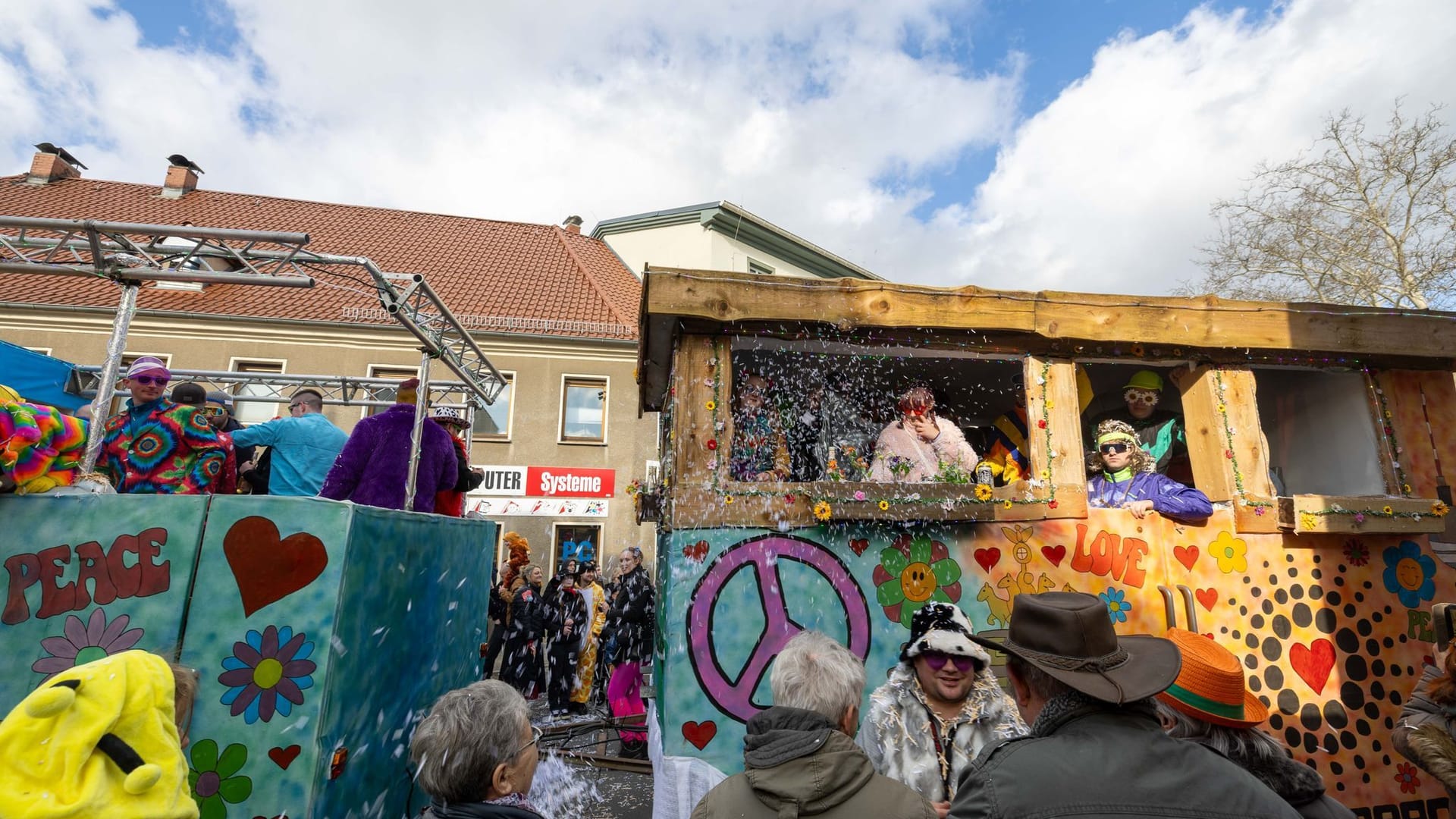 Menschen nehmen am Faschingsumzug in Radeburg teil, wobei mit zwei Wagen auch ein bisschen Loveparade-Gefühl vermittelt wird.