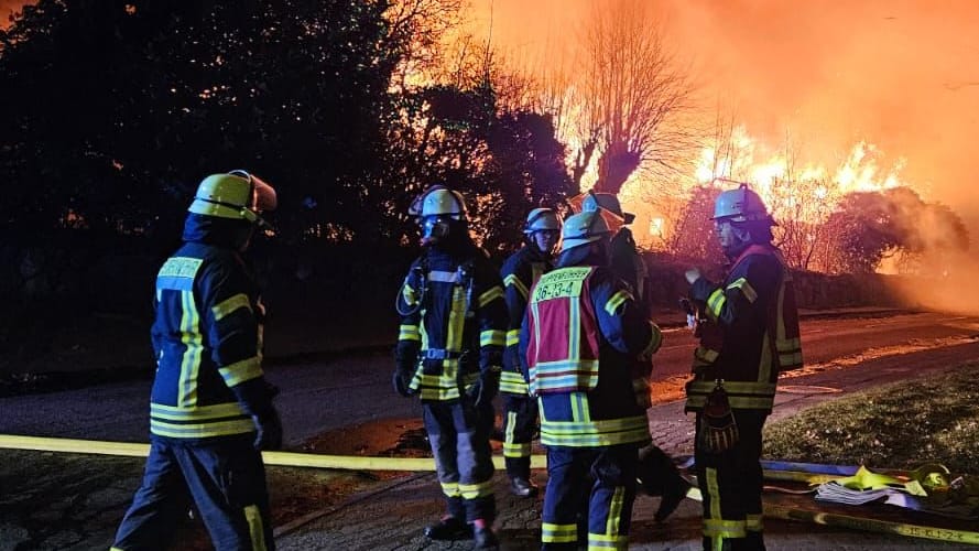 Feuerwehrleute stehen vor dem Großbrand in Dollern: Eine Scheune und zwei Wohnhäuser sind in der Nacht in Flammen aufgegangen.