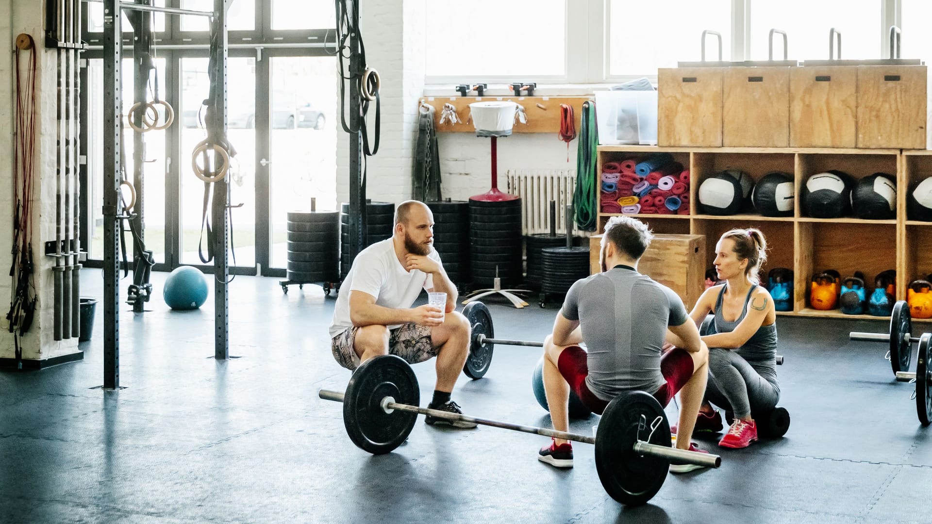 Drei Erwachsene mit Hanteln im Fitnessstudio: Bestimmte Sportarten können sich auf die Gefäßpolster am After auswirken.