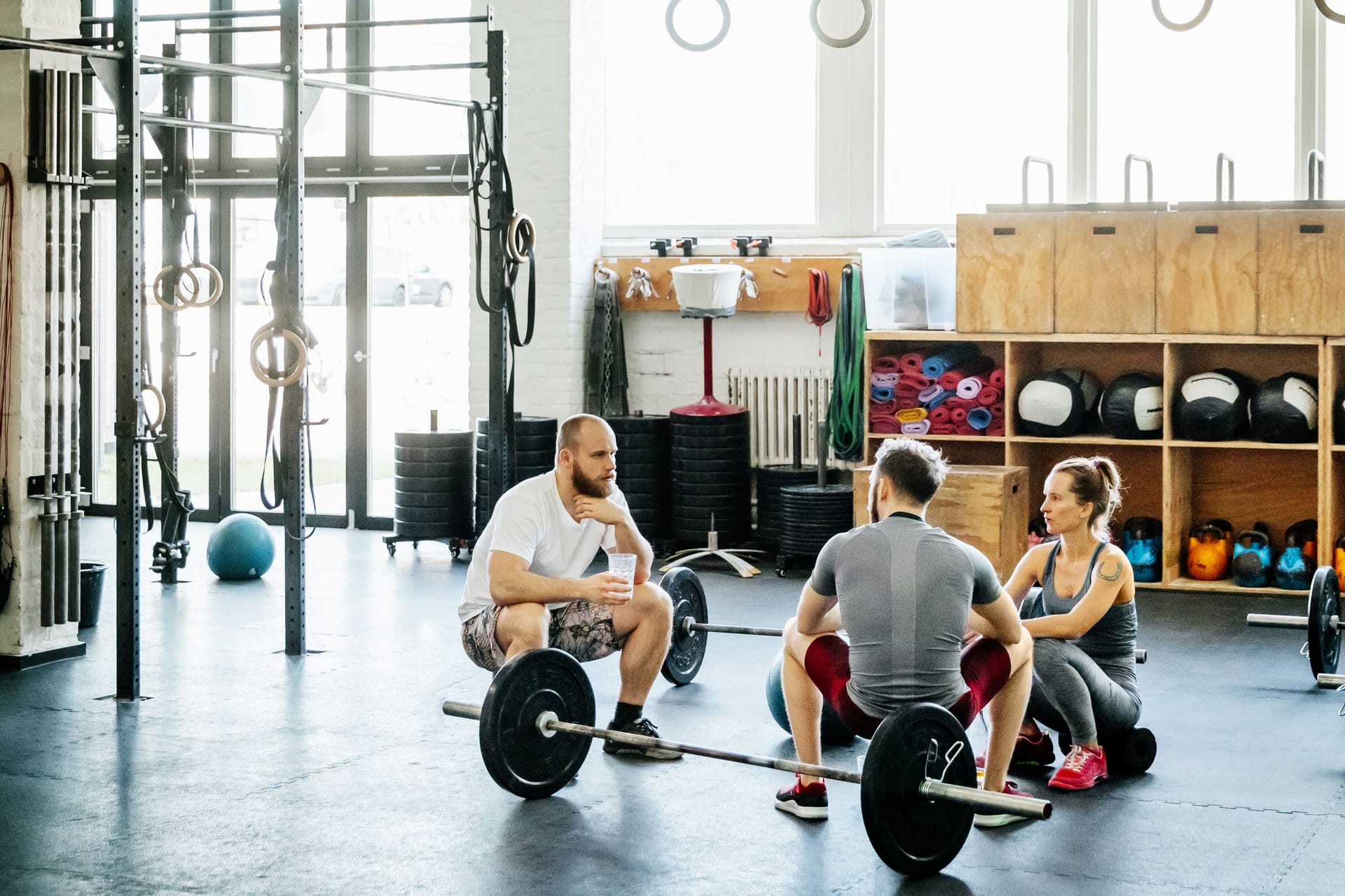 Drei Erwachsene mit Hanteln im Fitnessstudio: Bestimmte Sportarten können sich auf die Gefäßpolster am After auswirken.