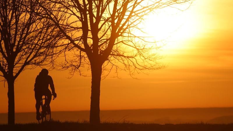 Ein Radfahrer ist am Morgen kurz nach Sonnenaufgang unterwegs, während sich der Himmel durch den Saharastaub in Orangetönen verfärbt hat.