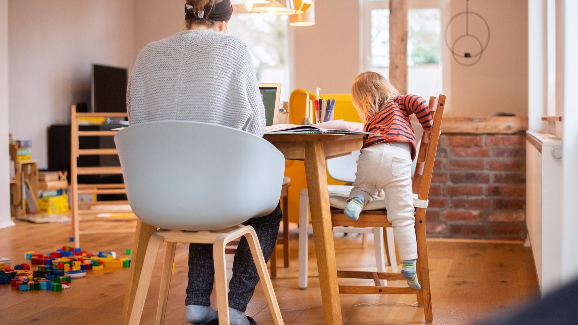 Zweijähriges Kind klettert auf einen Stuhl neben seiner Mutter