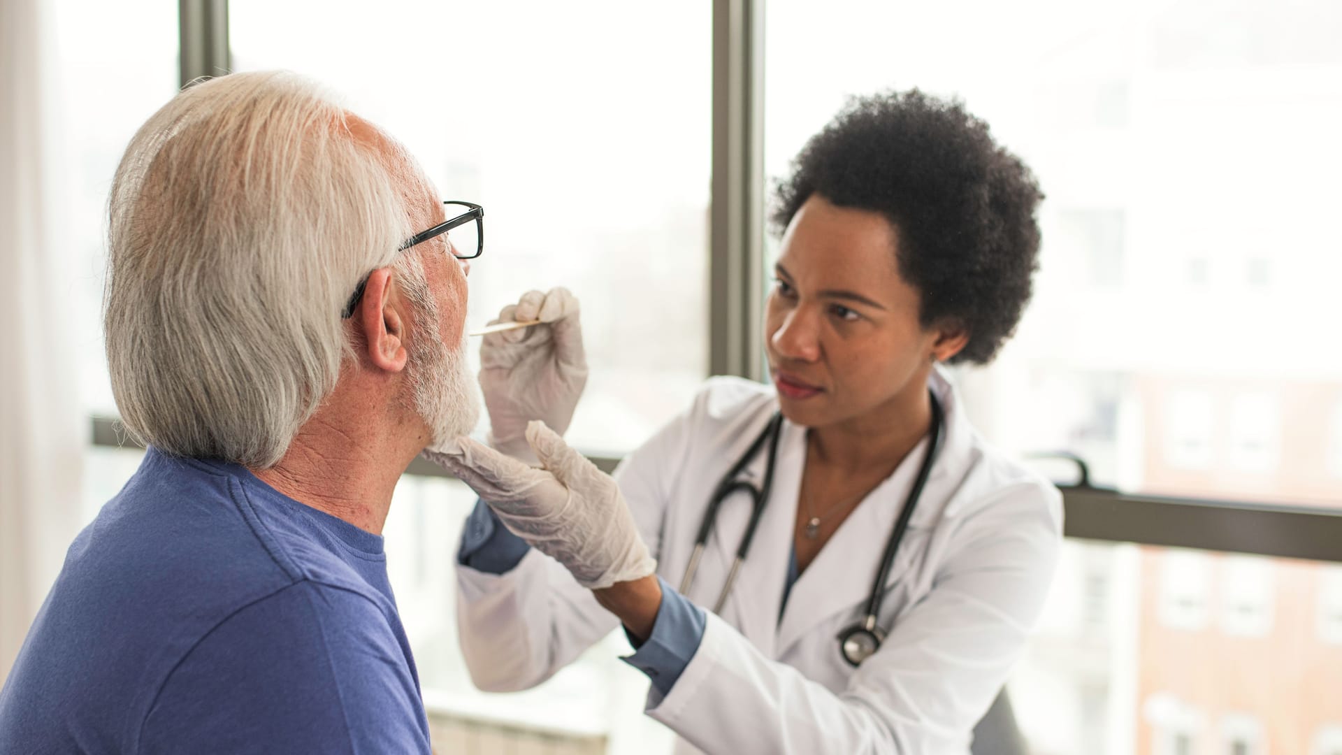 Ärztin untersucht den Mundraum eines Patienten: Zungenkrebs kann durch Veränderungen im Bereich der Zunge auffallen.