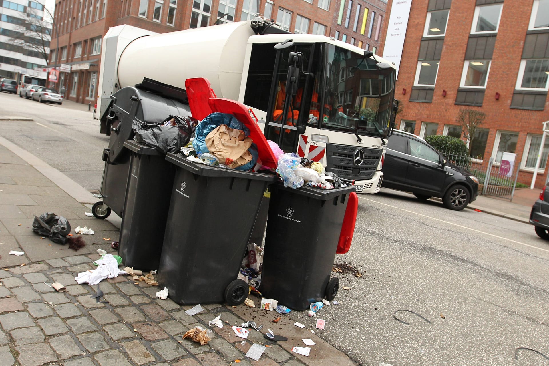 Müllwagen fährt an überfüllten Mülltonnen vorbei (Symbolbild): Droht in Hamburg wegen neuer Streiks ein Müll-Chaos?