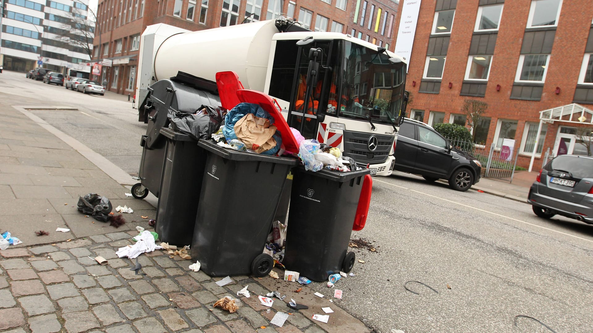 Müllwagen fährt an überfüllten Mülltonnen vorbei (Symbolbild): Droht in Hamburg wegen neuer Streiks ein Müll-Chaos?