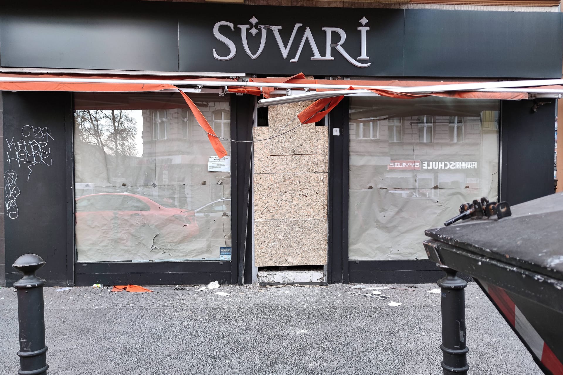 Berlin, Deutschland, 22.02.2025: Neukölln: Kugelbombe explodiert vor Geschäft in der Karl-Marx-Straße: Wenige Stunden nach dem Anschlag liegen noch Splitter vor dem Laden, die Tür wurde provisorisch versammelt