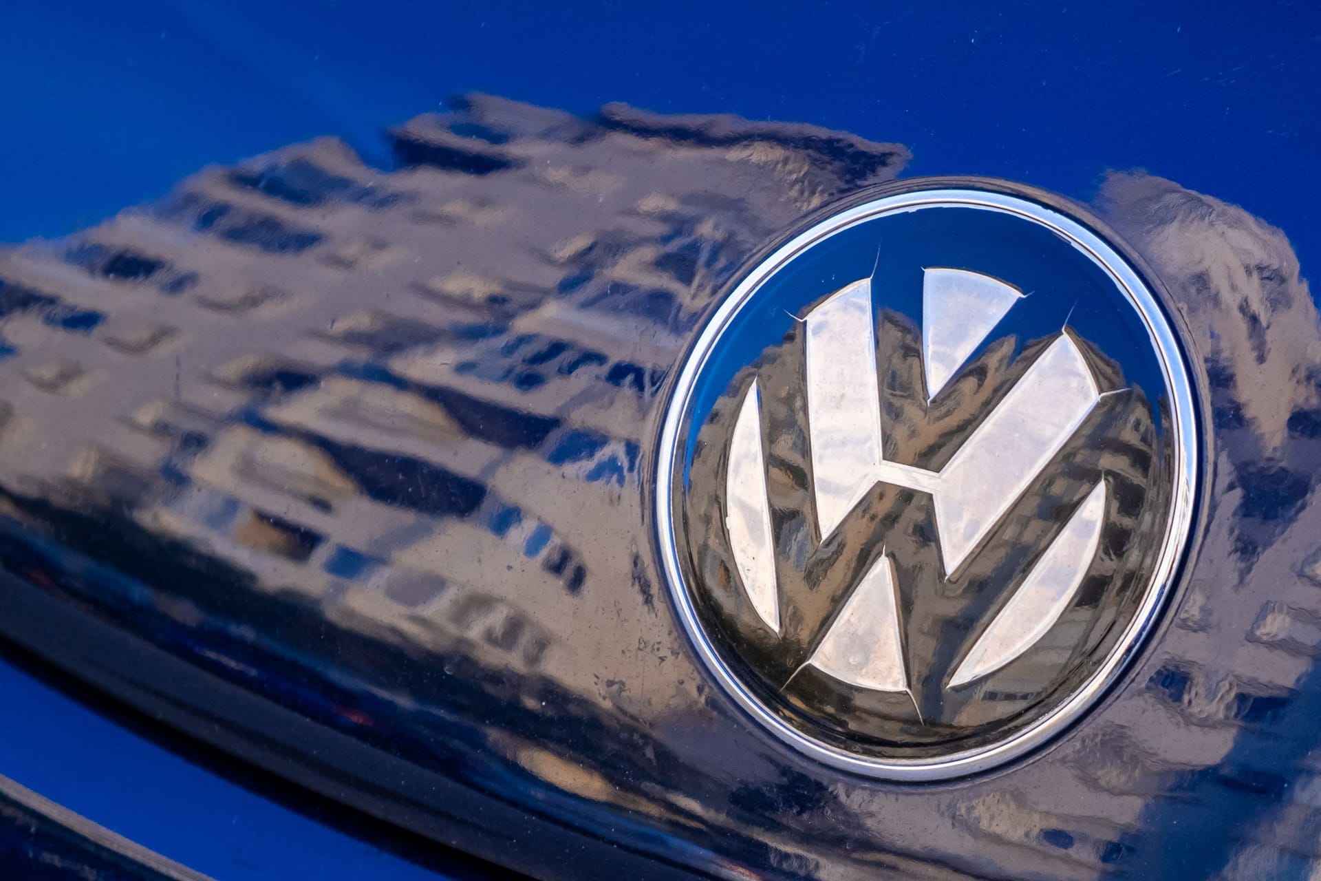 Volkswagen logo on a bright blue car, close up, city reflection