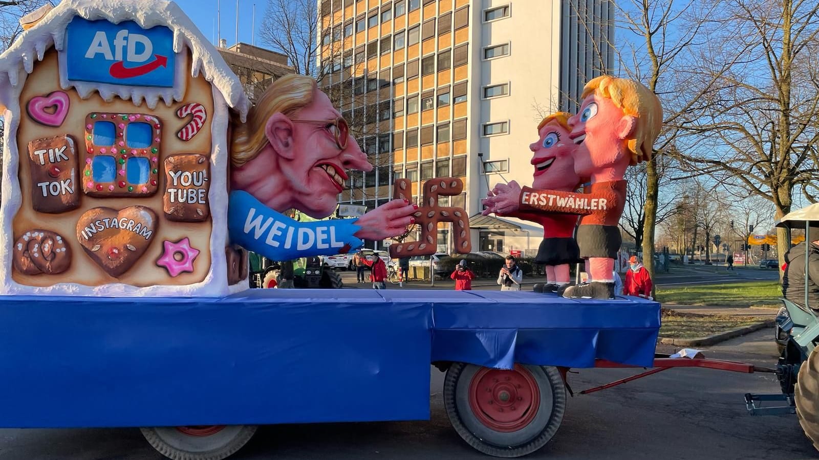 Alice Weidel verführt als "Hexe" Erstwähler: Die AfD-Chefin ist als Hexe aus "Hänsel und Gretel" zu sehen, wie sie aus ihrem Haus Lebkuchen in Hakenkreuz-Form verteilt. Tilly hat dabei mit Warzen im Gesicht von Weidel nicht gespart. Das Haus schmücken außerdem Lebkuchen mit den Aufschriften: "TikTok", "Instagram" und "Youtube". Auf der anderen Seite stehen die "Erstwähler", die bereitwillig in Weidels Arme laufen.