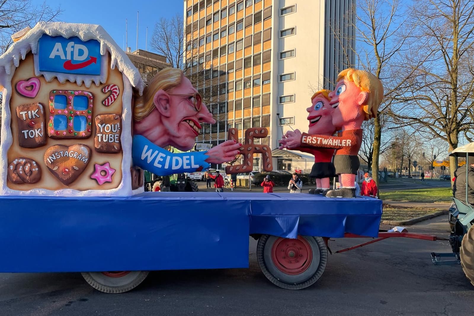 Alice Weidel verführt als "Hexe" Erstwähler: Die AfD-Chefin ist als Hexe aus "Hänsel und Gretel" zu sehen, wie sie aus ihrem Haus Lebkuchen in Hakenkreuz-Form verteilt. Tilly hat dabei mit Warzen im Gesicht von Weidel nicht gespart. Das Haus schmücken außerdem Lebkuchen mit den Aufschriften: "TikTok", "Instagram" und "Youtube". Auf der anderen Seite stehen die "Erstwähler", die bereitwillig in Weidels Arme laufen.