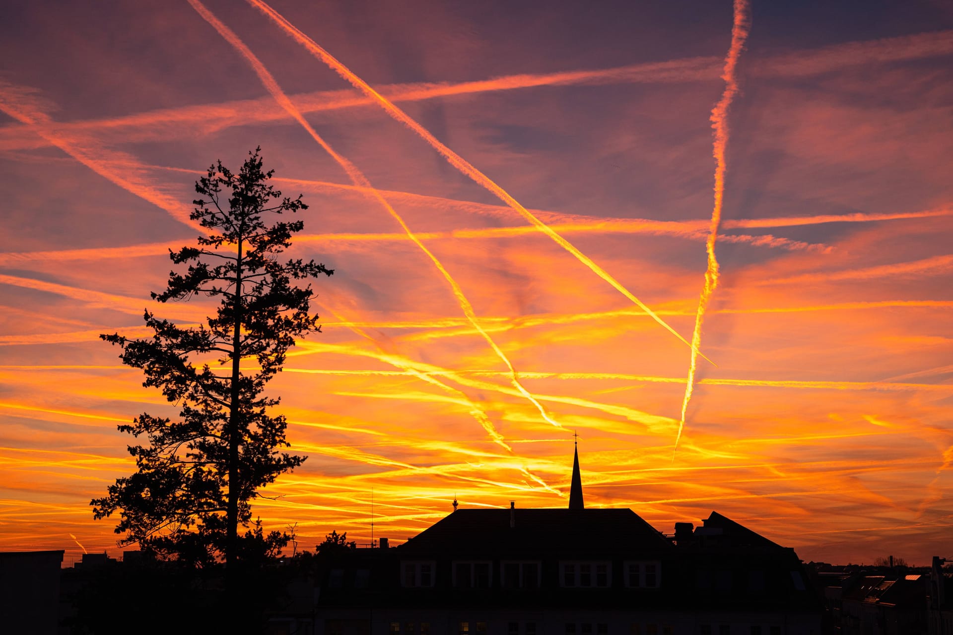 Stimmungsvoller Sonnenuntergang zur Goldenen Stunde mit Kondensstreifen am roten Abendhimmel ueber den Daechern von Berlin-Charlottenburg