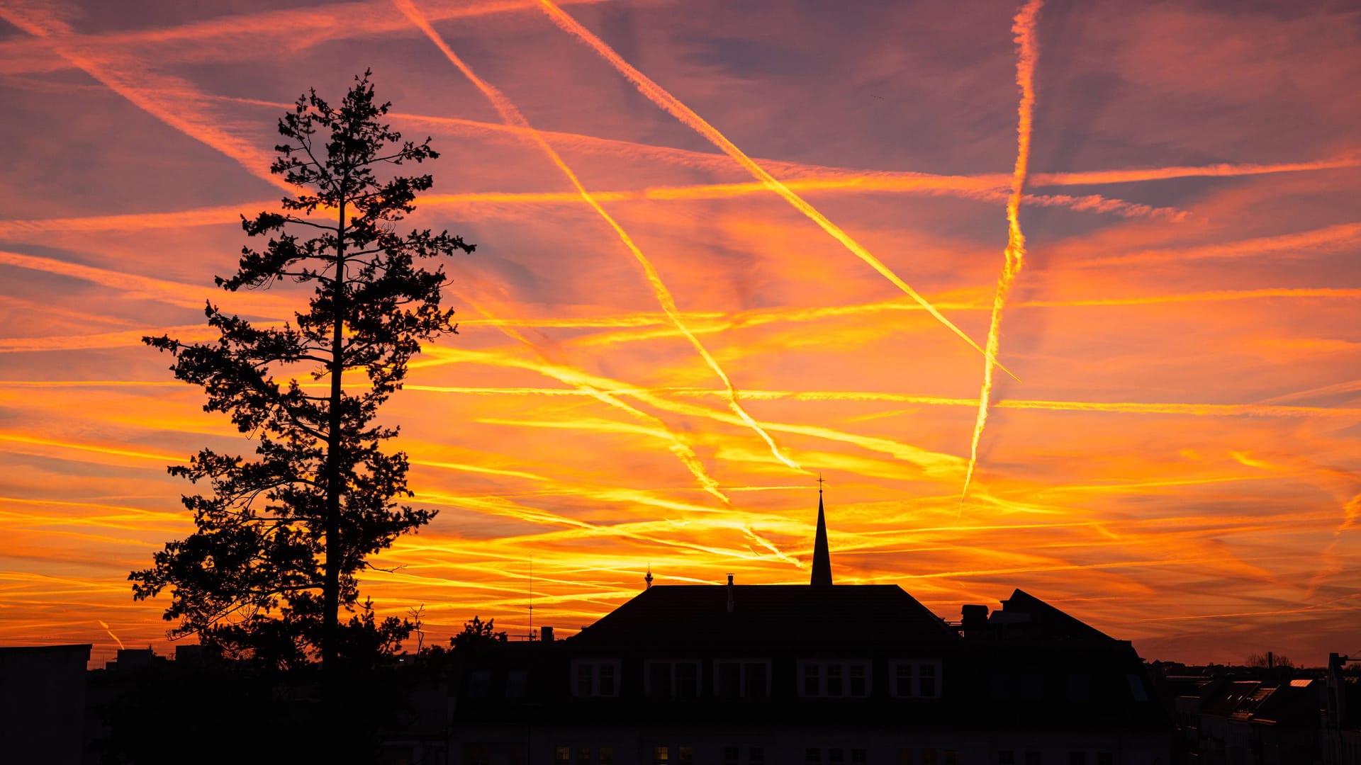 Stimmungsvoller Sonnenuntergang zur Goldenen Stunde mit Kondensstreifen am roten Abendhimmel ueber den Daechern von Berlin-Charlottenburg