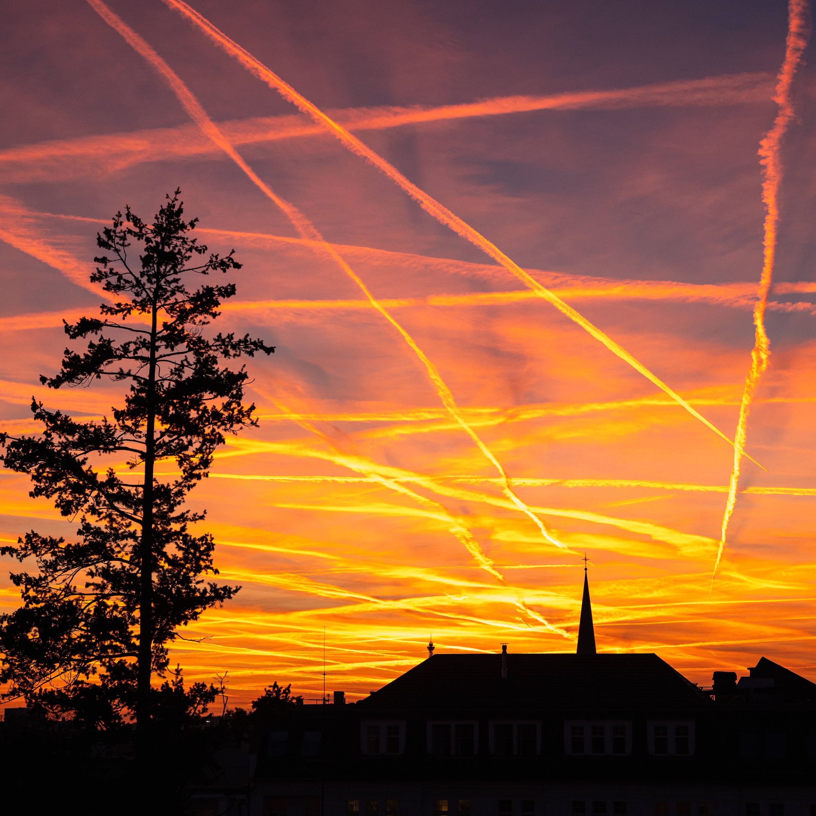 Stimmungsvoller Sonnenuntergang zur Goldenen Stunde mit Kondensstreifen am roten Abendhimmel ueber den Daechern von Berlin-Charlottenburg