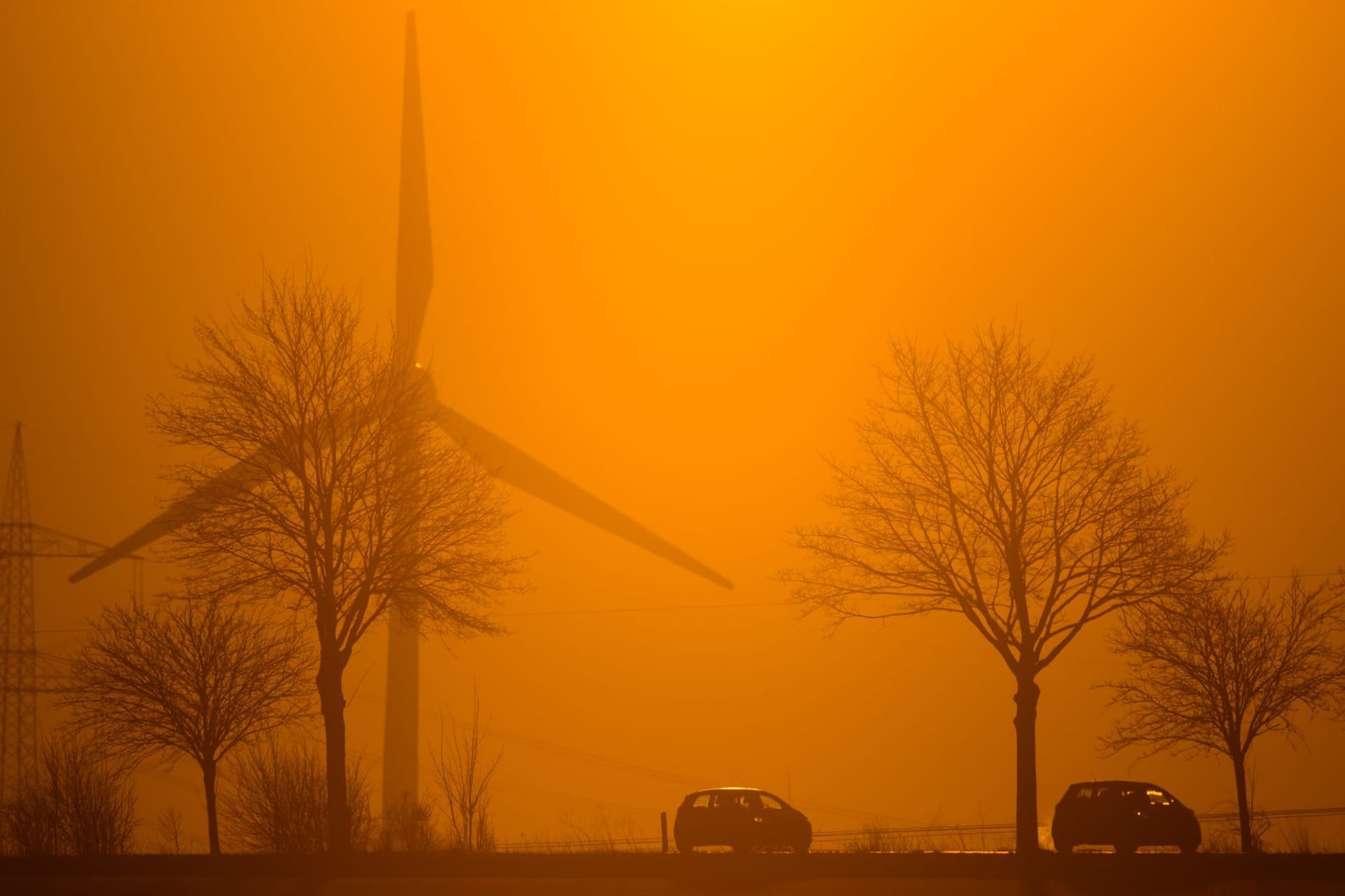 Autos fahren im Licht der aufgehenden Sonne über eine Landstraße in der Region Hannover. Dahinter ist ein Windrad zu sehen.