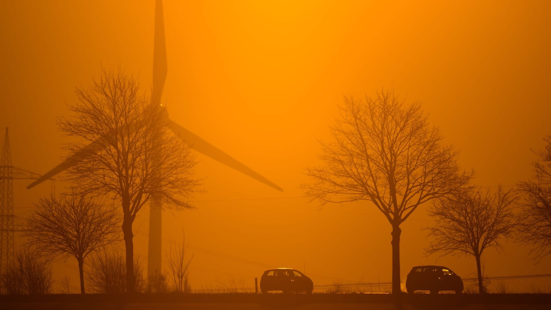 Autos fahren im Licht der aufgehenden Sonne über eine Landstraße in der Region Hannover. Dahinter ist ein Windrad zu sehen.