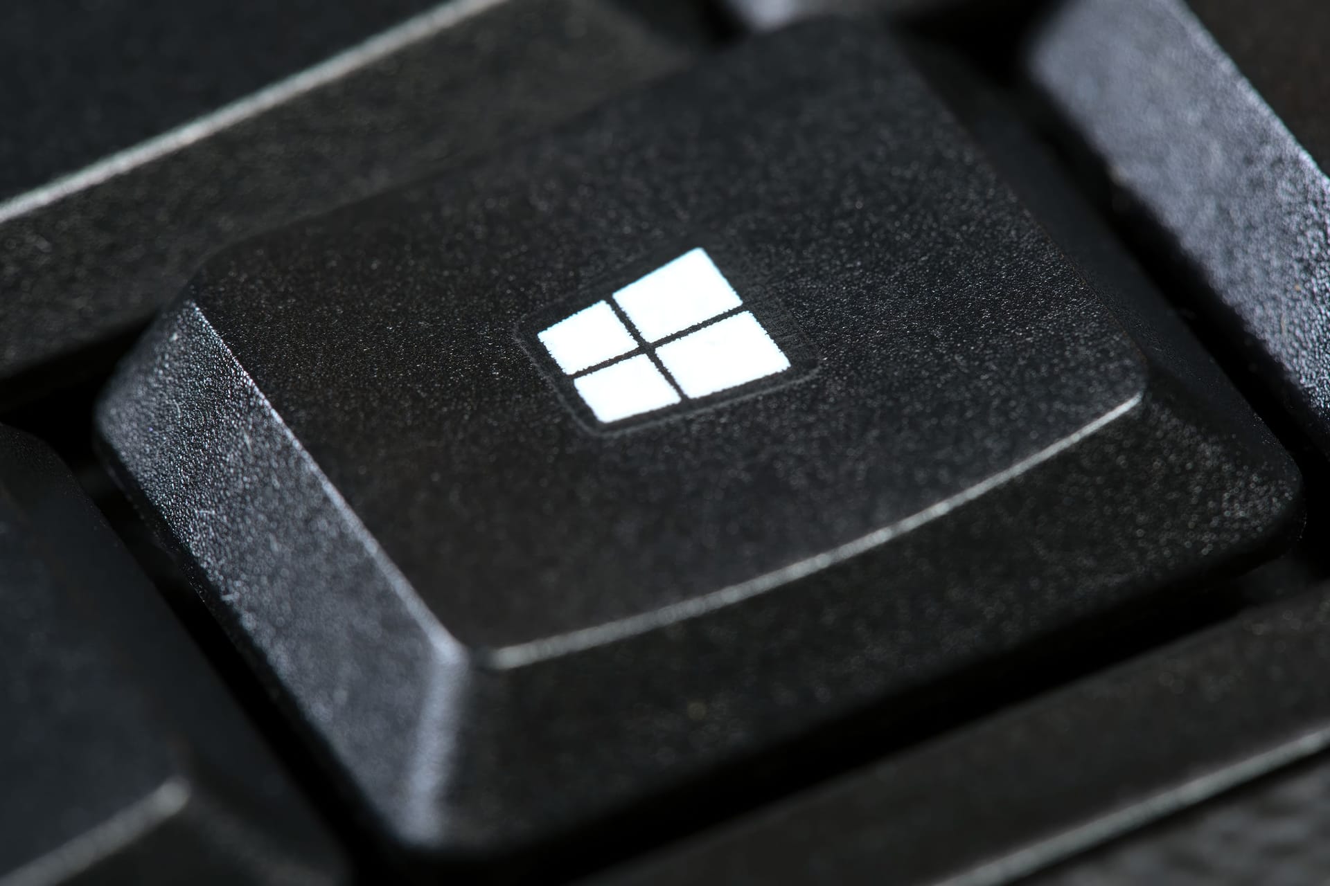 Microsoft Windows OS logo, operating system key on a simple black desktop PC computer keyboard, macro, extreme closeup. OS button brand detail. Operating systems concept