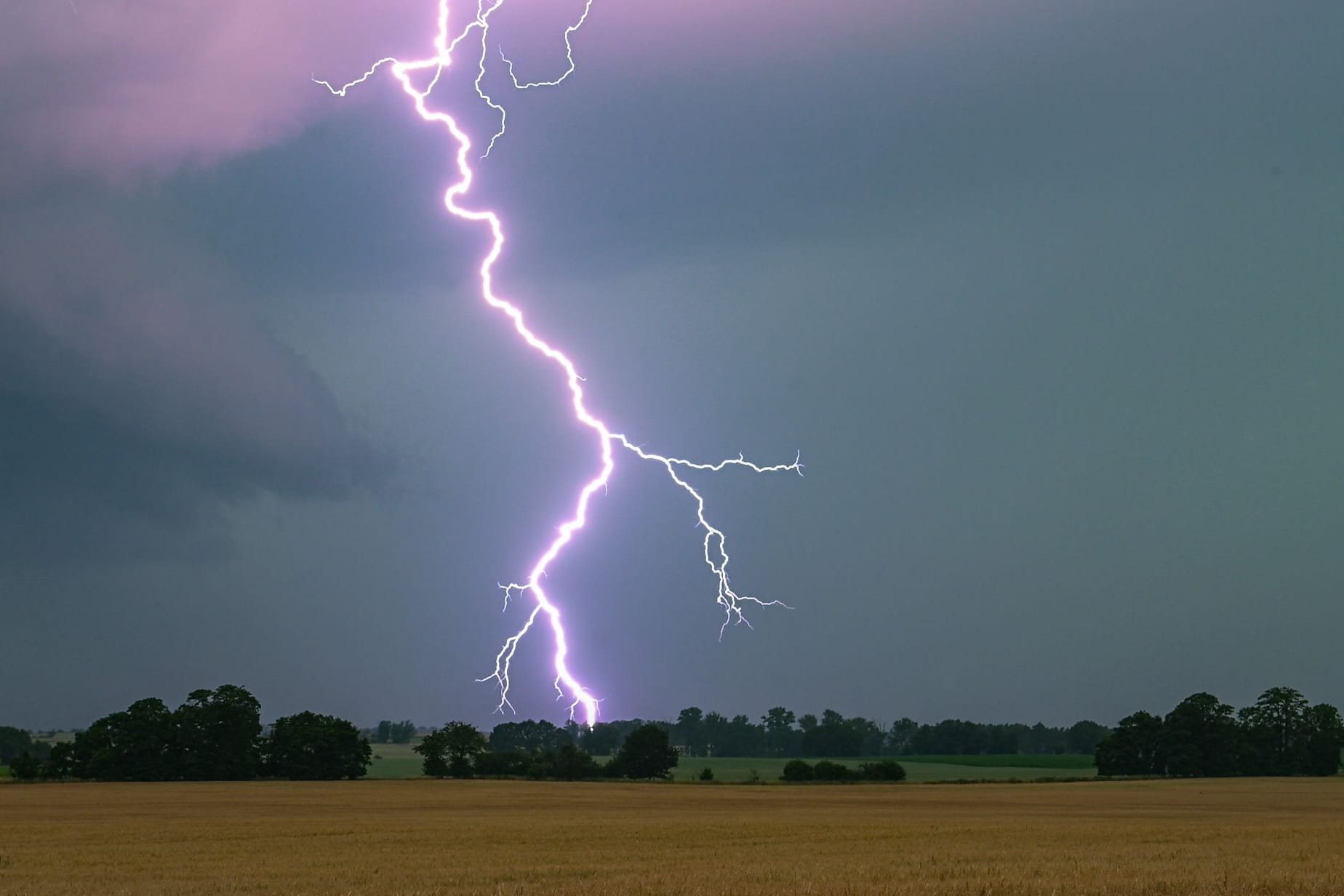Gewitterblitz über einem Feld (Symbolbild): Am Wochenende wird ein Wetterumschwung mit starkem Regen und Gewittern erwartet.