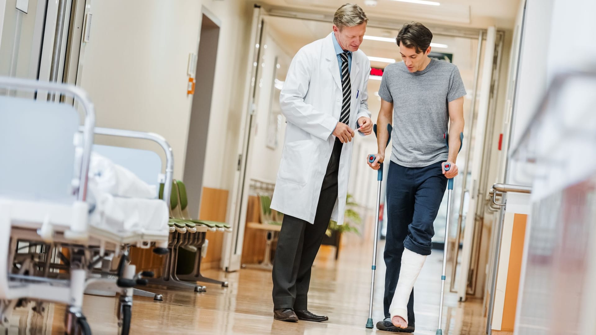 Mann mit gebrochenem Fuß spricht mit Arzt im Flur des Krankenhauses