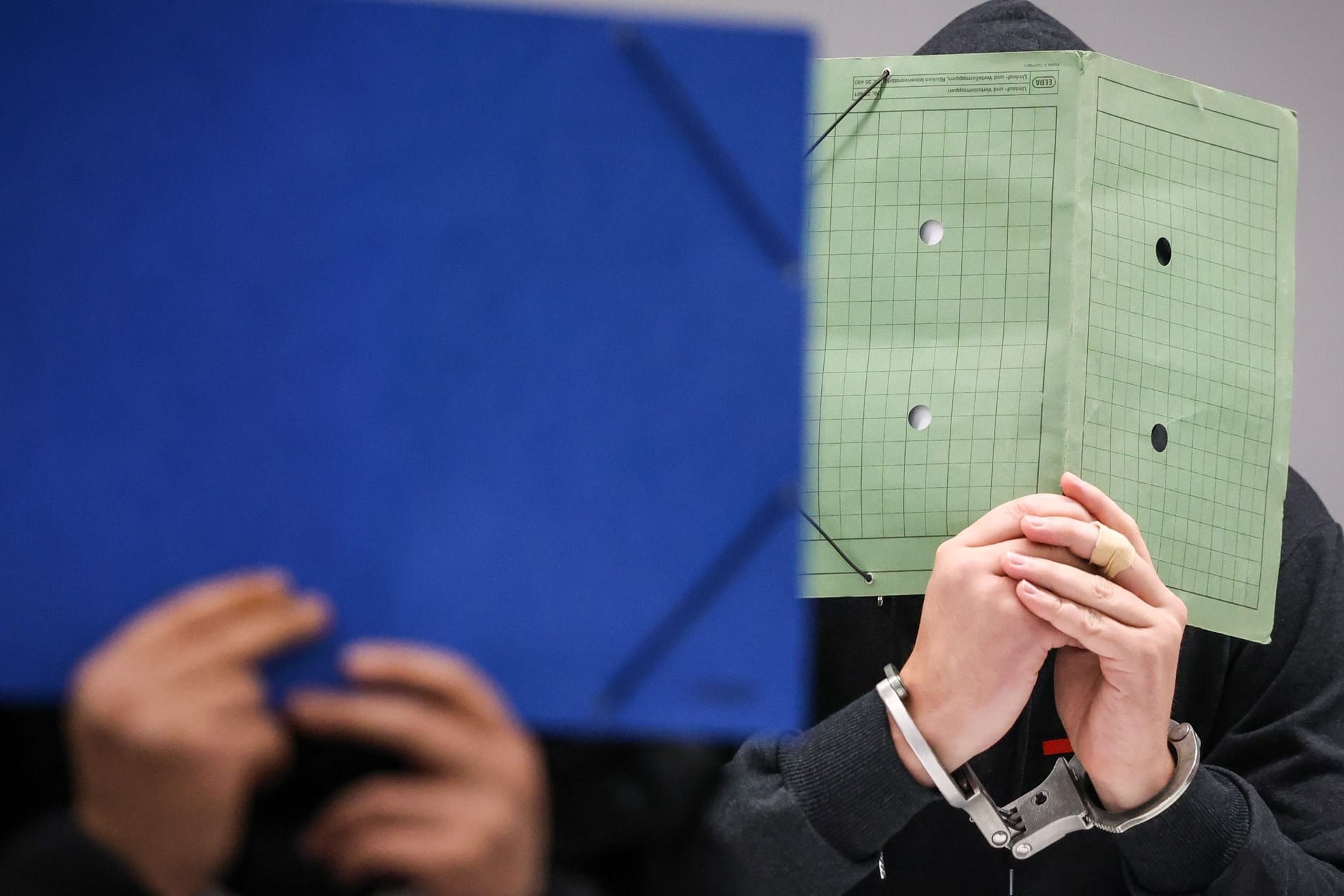Zwei Angeklagte halten sich Mappen vor die Gesichter (Archivbild): Gegen neun Männer aus einer Kokain-Bande soll am Dienstag das Urteil fallen.