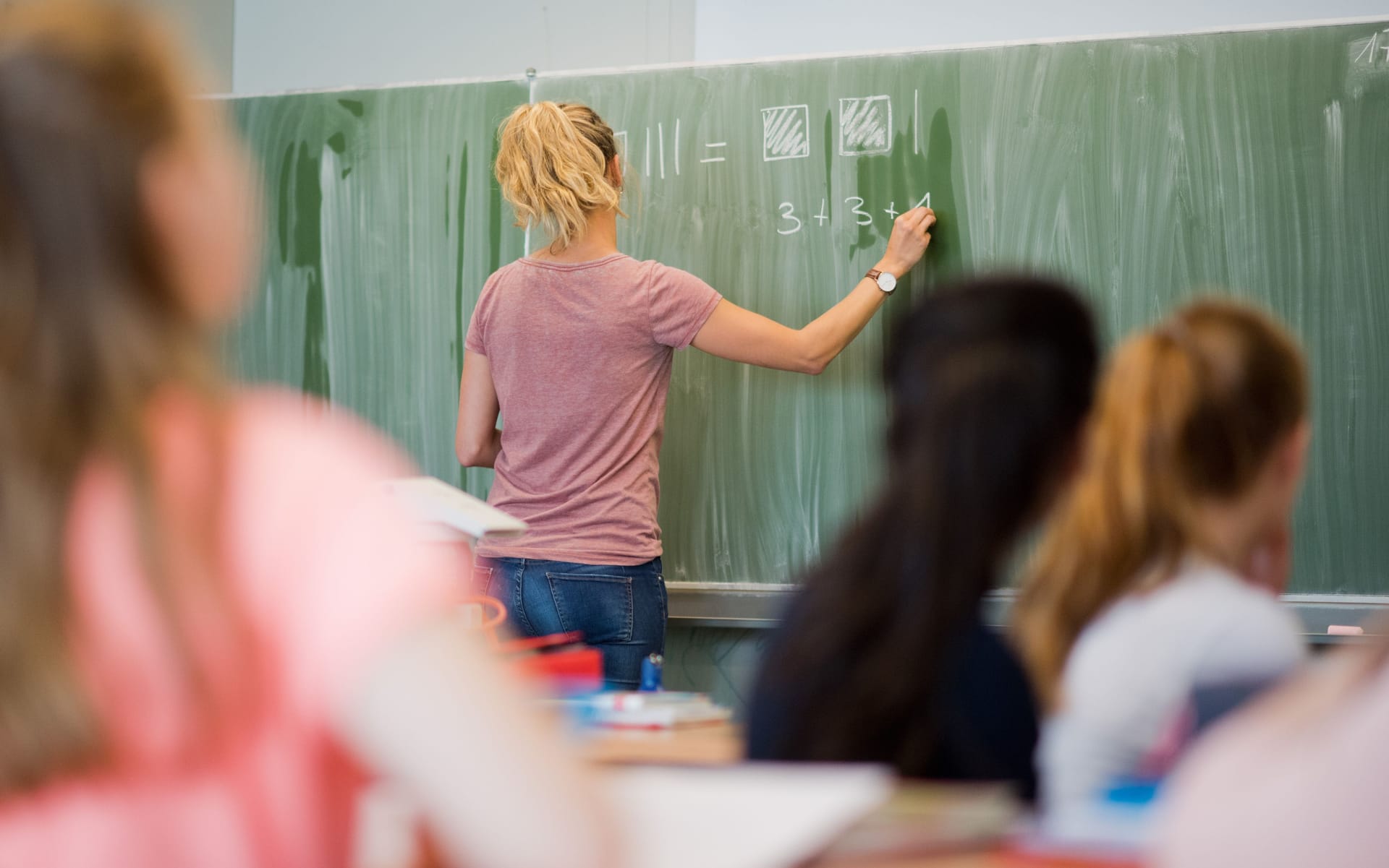 Eine Lehrerin schreibt etwas an eine Tafel: Aus Sicht von Juristen bedürfen Lehrer keiner besonderen Absicherung durch den Beamtenstatus.