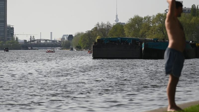Ein Mann steht in Badehose an der Spree auf Berlin-Stralau und genießt die Sonne. Im Hintergrund ist der Fernsehturm und die Elsenbrücke. (zu dpa: «Bezirk Mitte möchte Baden in Spree gerne wieder ermöglichen»)