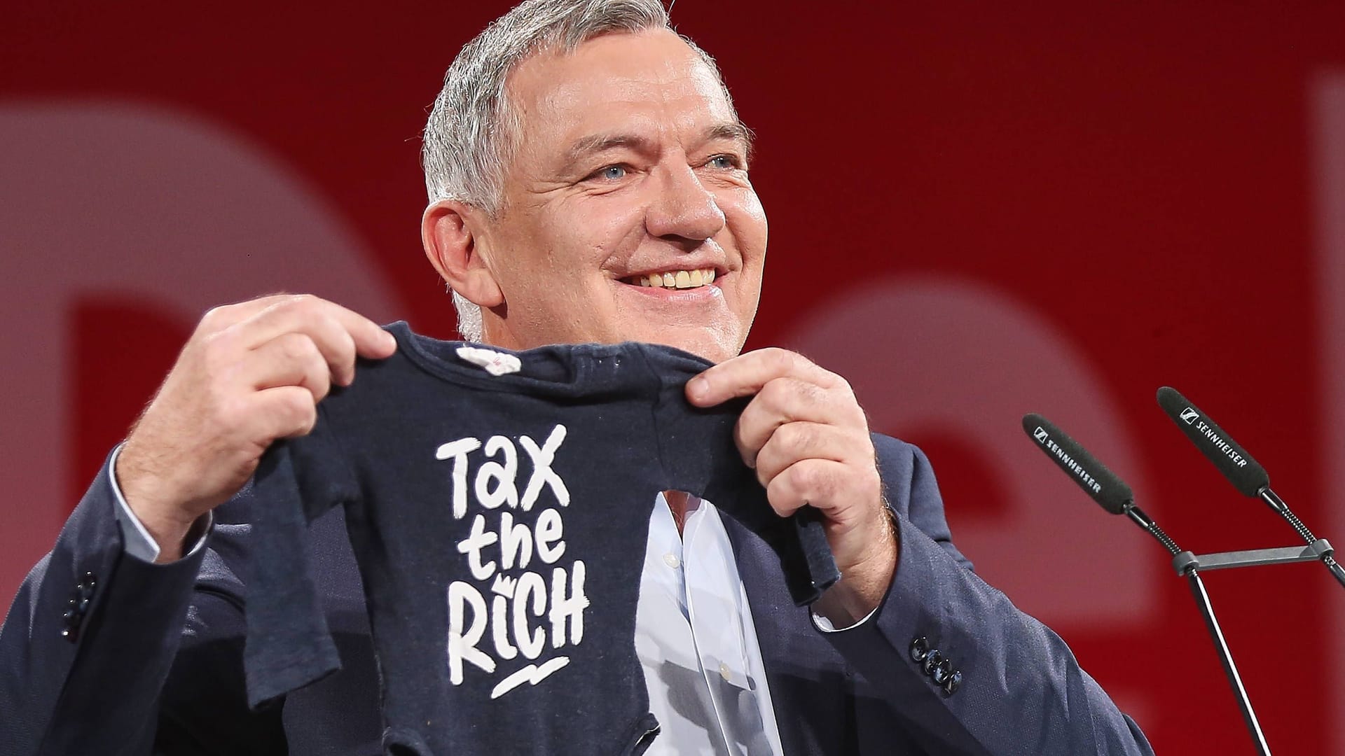Linkenchef Jan van Aken zeigt einen Baby-Strampler mit der Aufschrift "Besteuert die Reichen", weil er Anfang des Jahres Opa geworden ist (Archivbild): Die Linke will Vermieter dazu zwingen, überhöhte Heizrechnungen zurückzuzahlen.