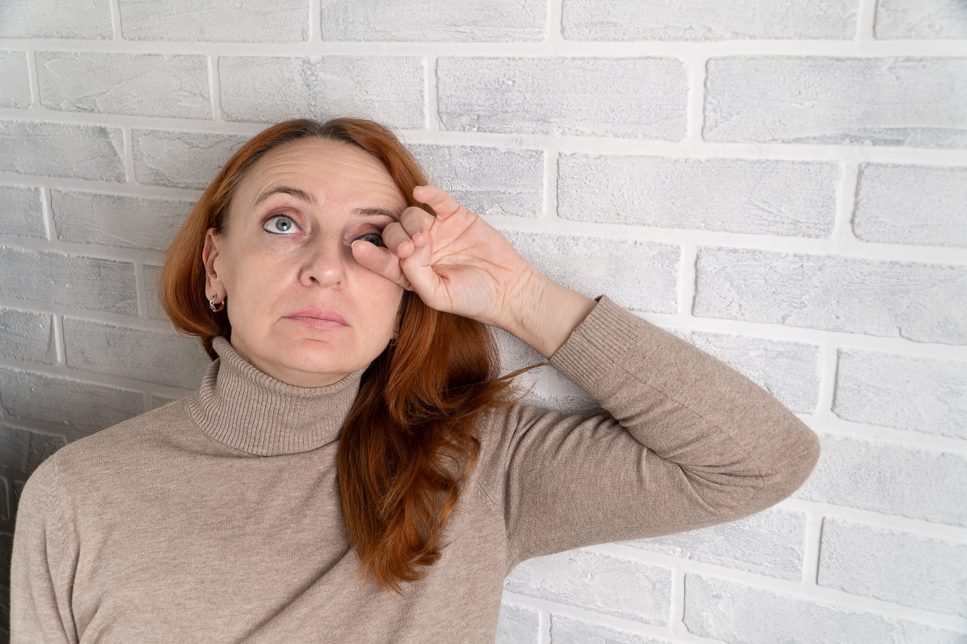 Frau fasst sich an ihr linkes Auge: Ein Gerstenkorn entsteht durch Bakterien.
