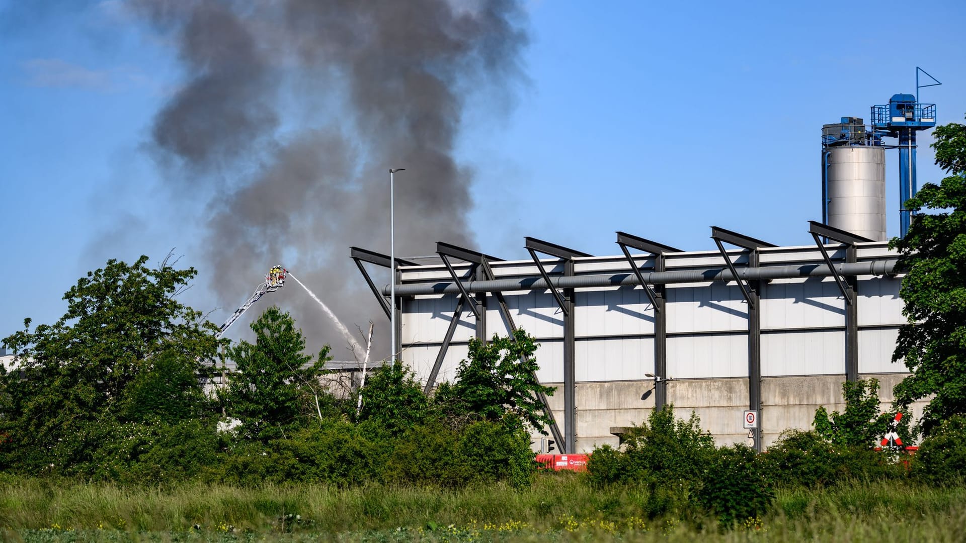 23.05.2025, Sachsen, Dresden: Die Feuerwehr ist mit den Löscharbeiten bei einem Brand auf einem Wertstoffhof beschäftigt. Seit den frühen Morgenstunden brenne eine rund 120 Quadratmeter große Halle, teilte die Leitstelle mit. In der Halle gelagerte Sortierreste stünden in Flammen. Das Feuer habe das gesamte Gebäude erfasst und führe zu einer starken Rauchentwicklung. Foto: Robert Michael/dpa
