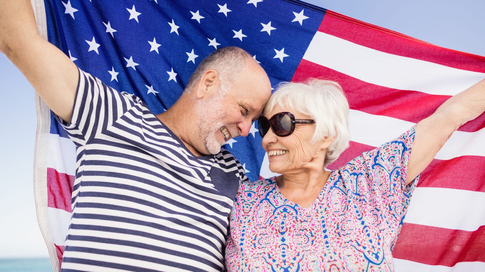 Seniorenpaar hält eine US-Flagge am Strand Seniorenpaar hält eine US-Flagge am Strand