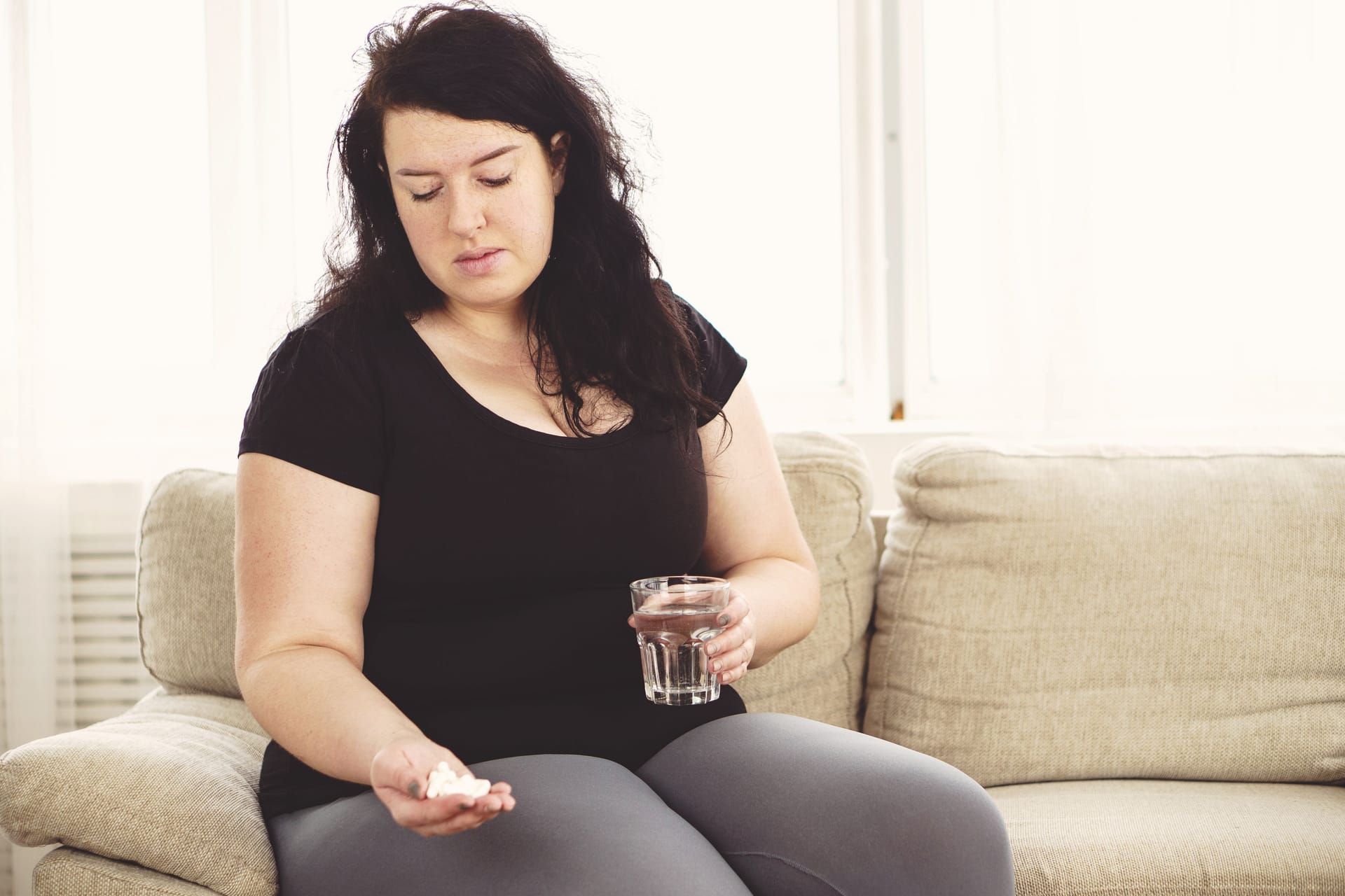 Übergewichtige Frau mit Tabletten und einem Glas Wasser in den Händen: Es gibt verschiedene Wirkstoffe zur Behandlung von Adipositas.