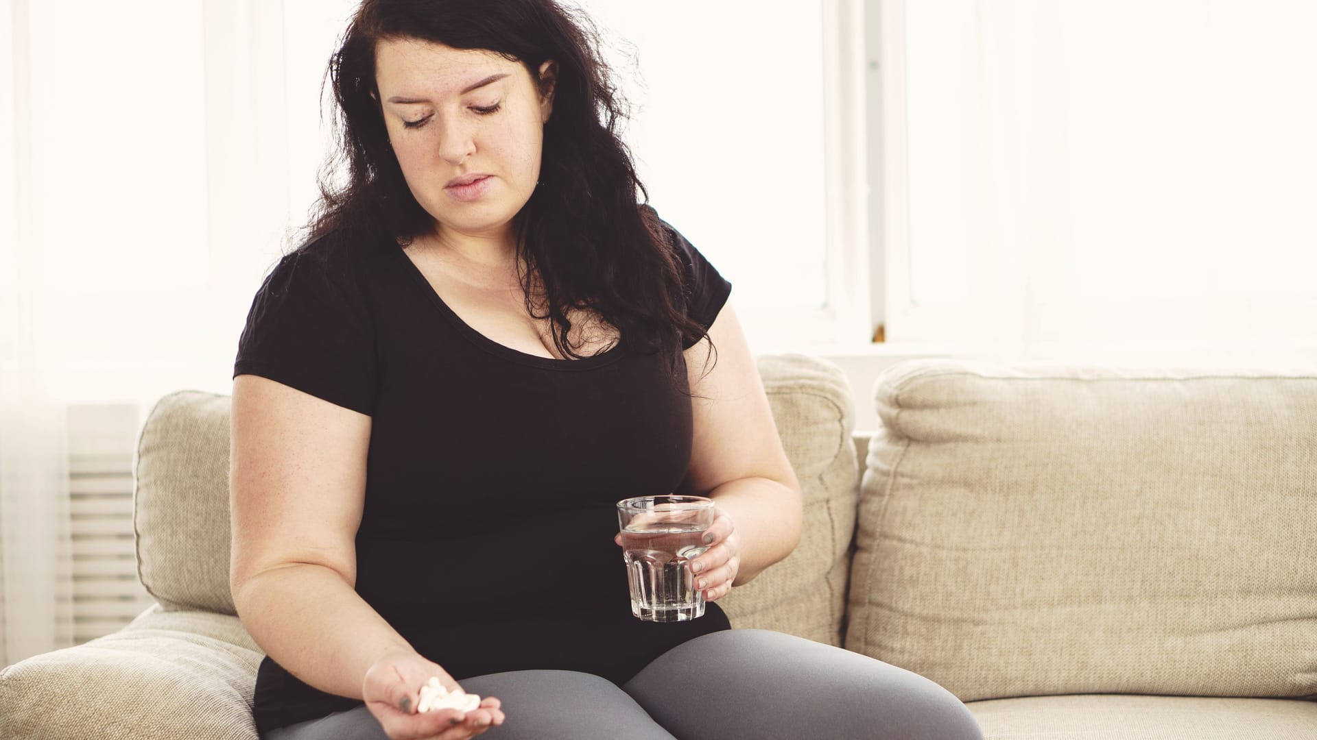 Übergewichtige Frau mit Tabletten und einem Glas Wasser in den Händen: Es gibt verschiedene Wirkstoffe zur Behandlung von Adipositas. Übergewichtige Frau mit Tabletten und einem Glas Wasser in den Händen: Es gibt verschiedene Wirkstoffe zur Behandlung von Adipositas.