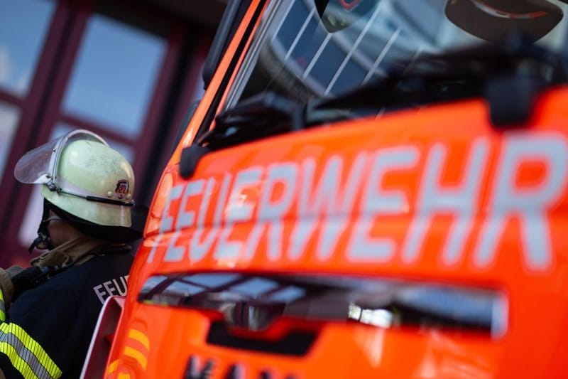 Eine Einsatzkraft der Feuerwehr steht neben einem Einsatzfahrzeug der Feuerwehr. (Symbolbild)
