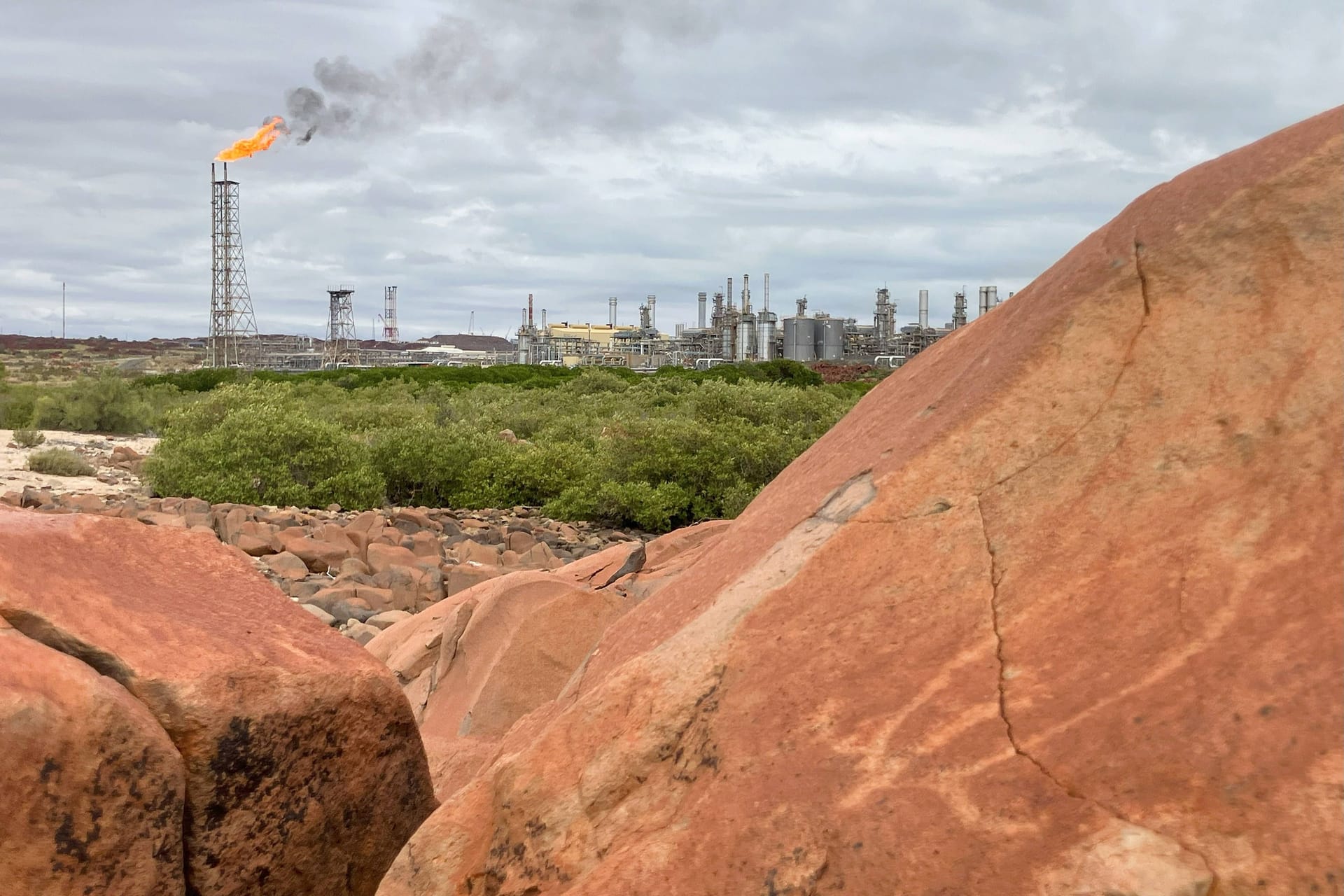 Ein Murujuga-Felsen mit Schildkrötendarstellung: Im Hintergrund brennt die Flamme einer Raffinerie.
