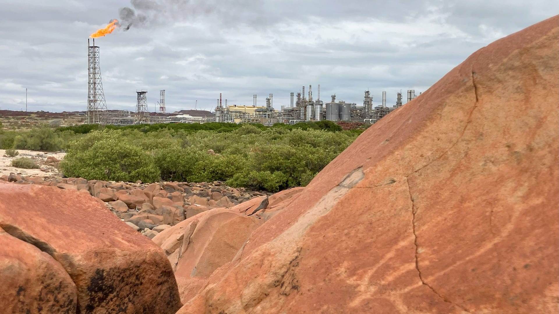 Ein Murujuga-Felsen mit Schildkrötendarstellung: Im Hintergrund brennt die Flamme einer Raffinerie.