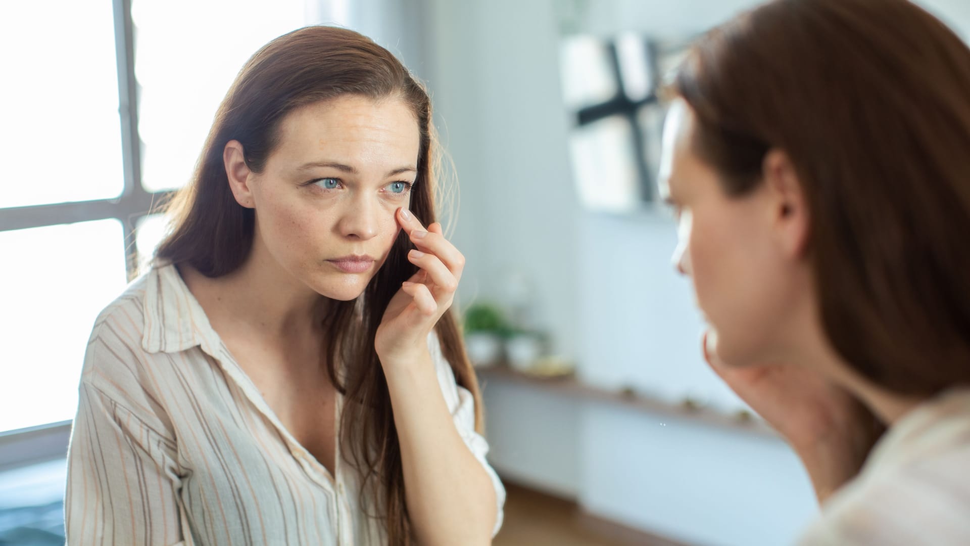 Eine Frau inspiziert ihr Auge im Spiegel: Für glasige, tränende Augen kann es viele Gründe geben.