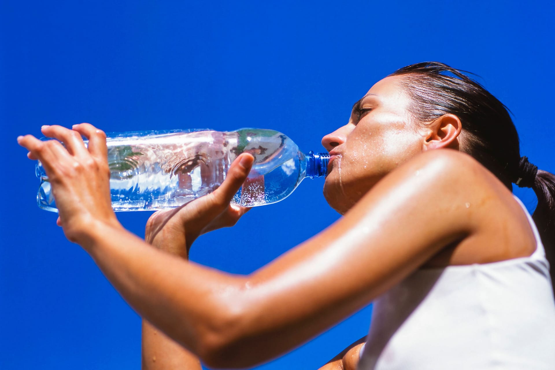 Frau trinkt Wasser unter blauem Himmel: Sengende Hitze könnte den Sommer 2025 in einen Katastrophensommer voller Extremwetter verwandeln.