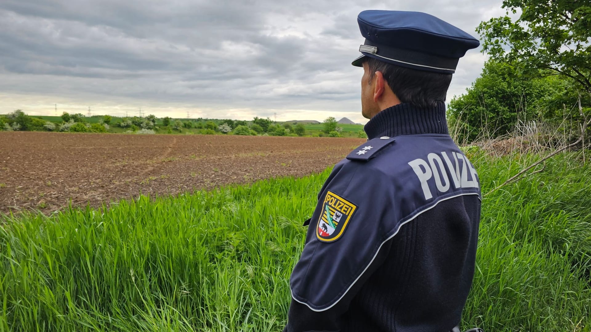 Ein Polizist der Polizeiinspektion Halle steht am Fundort an einem Feld am Rande von Benndorf: Ob es sich tatsächlich um die Leiche von Sandra K. handelt, wird noch untersucht.