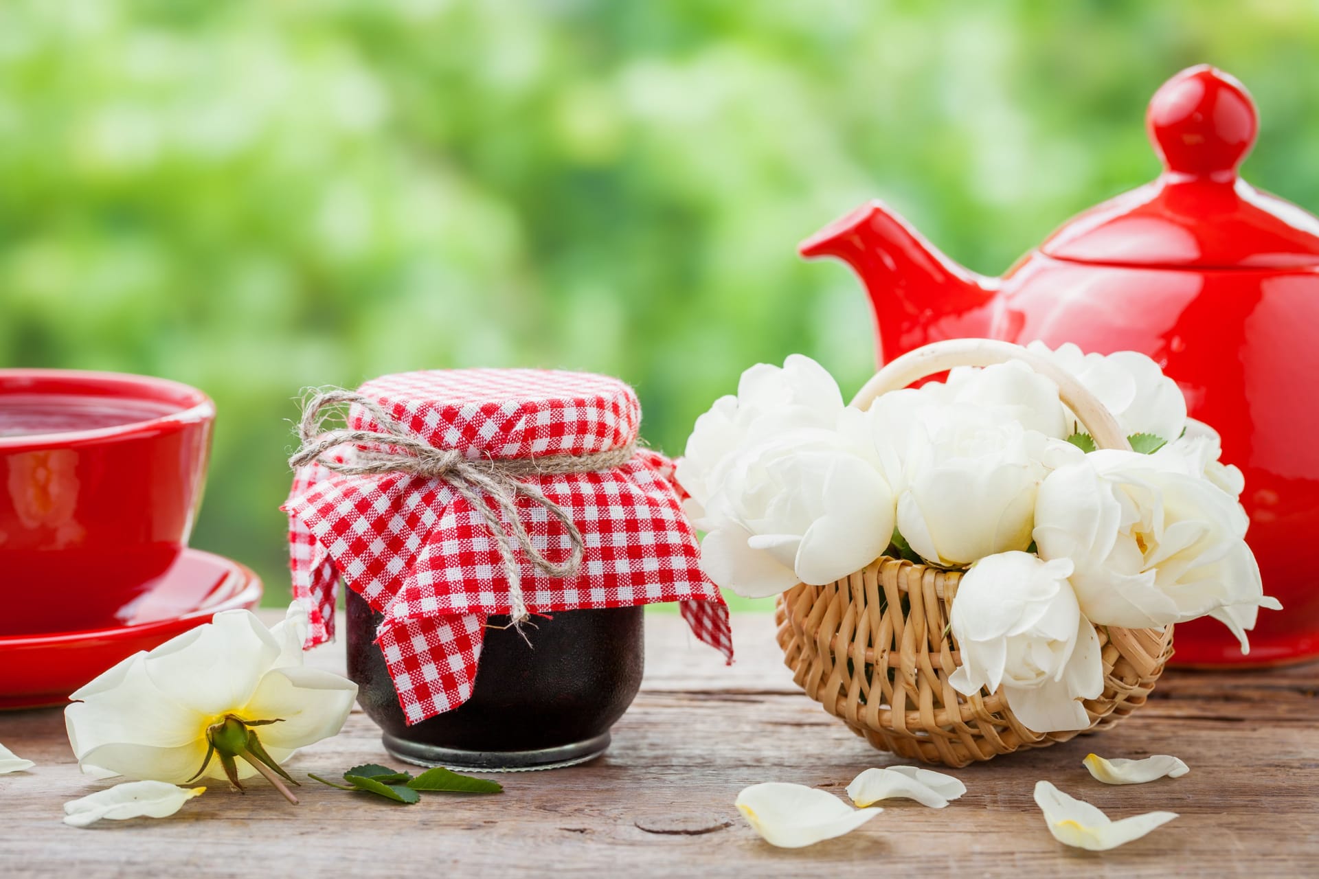 Red teapot, jars of jam, basket with roses bunch and tea cup.