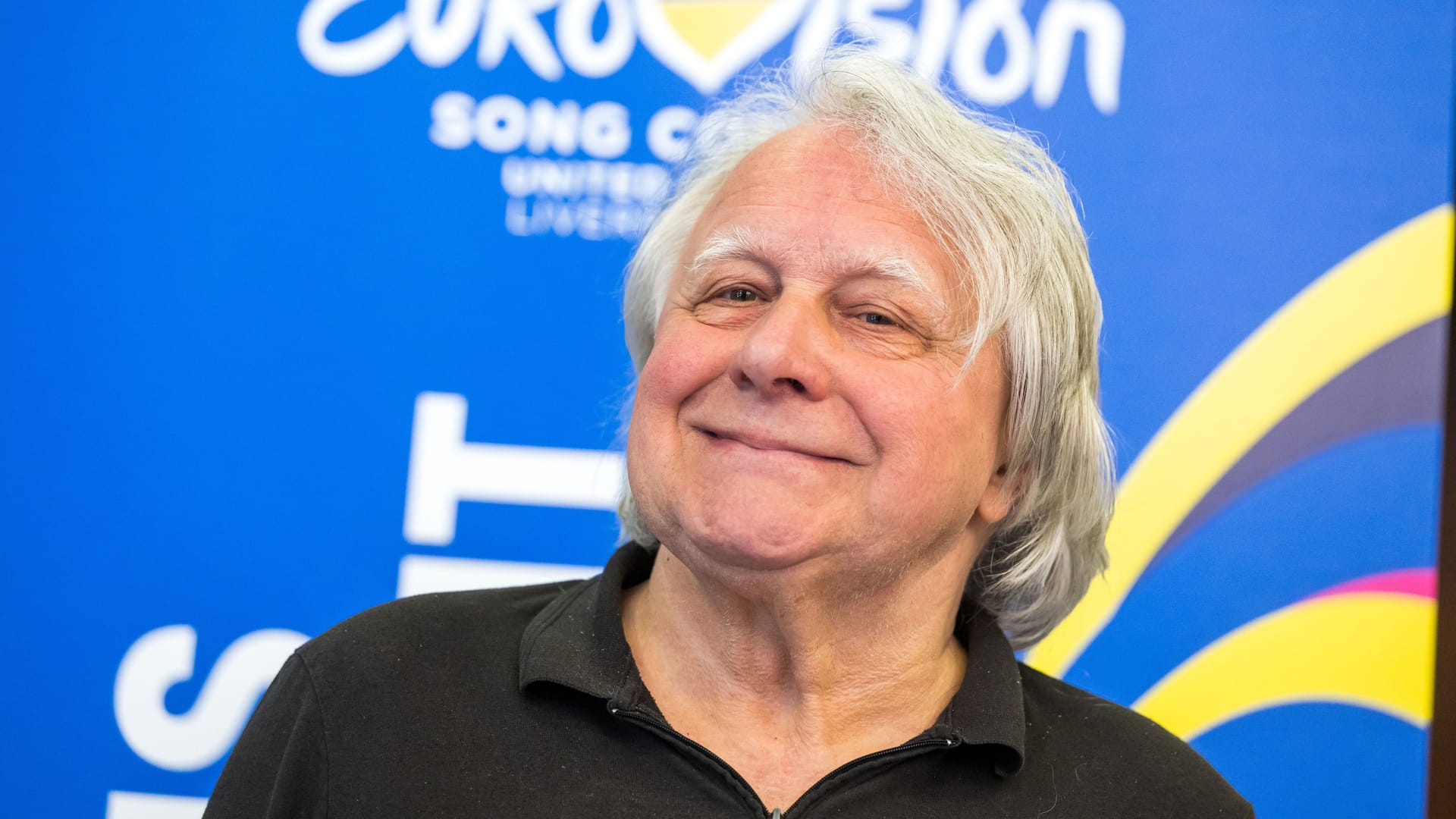 Peter Urban steht vor dem ESC-Logo (Symbolbild): Der 75-Jährige musste einen TV-Auftritt nach einem schweren Sturz absagen. Peter Urban steht vor dem ESC-Logo (Symbolbild): Der 75-Jährige musste einen TV-Auftritt nach einem schweren Sturz absagen.