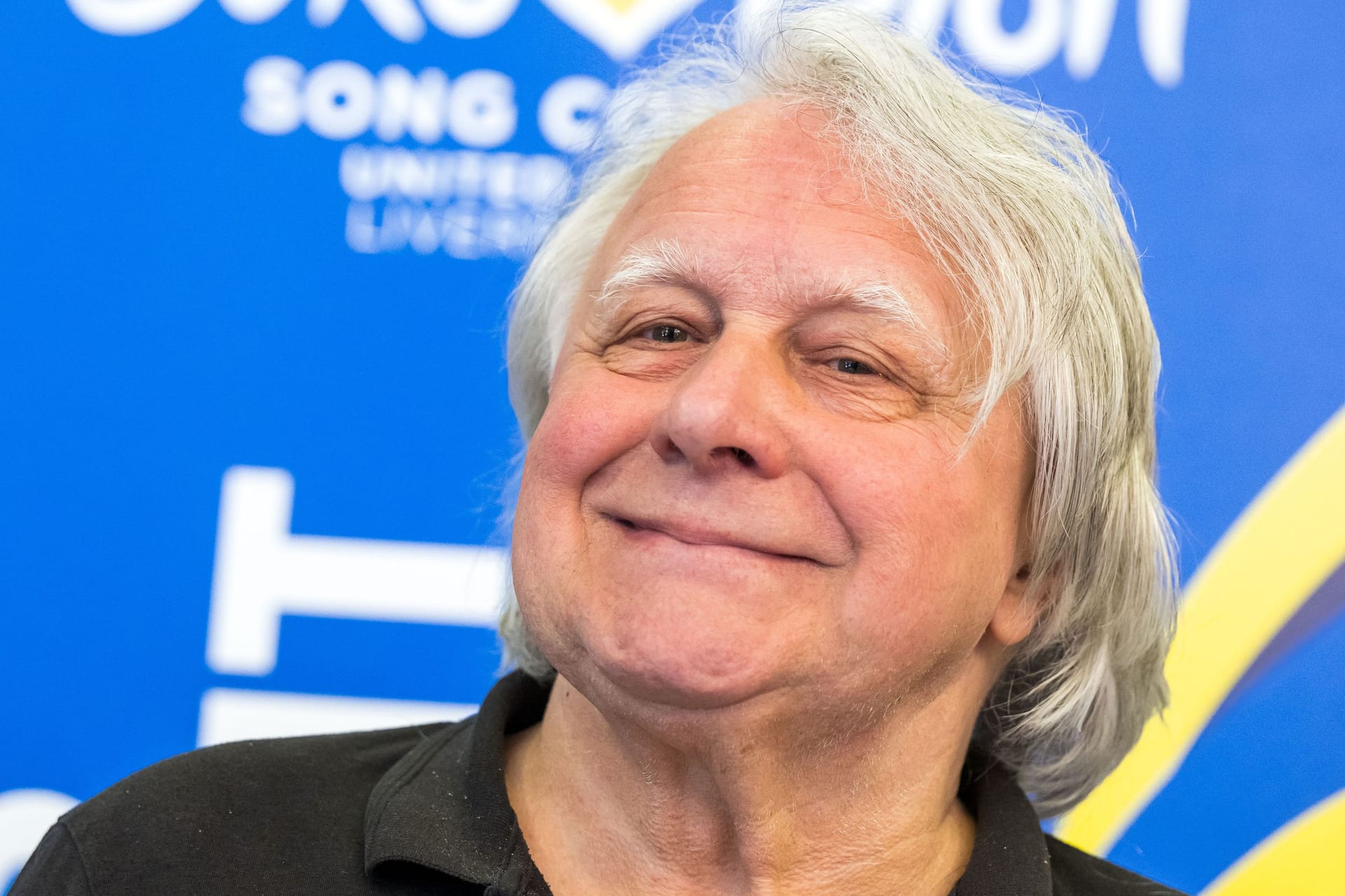 Peter Urban steht vor dem ESC-Logo (Symbolbild): Der 75-Jährige musste einen TV-Auftritt nach einem schweren Sturz absagen.