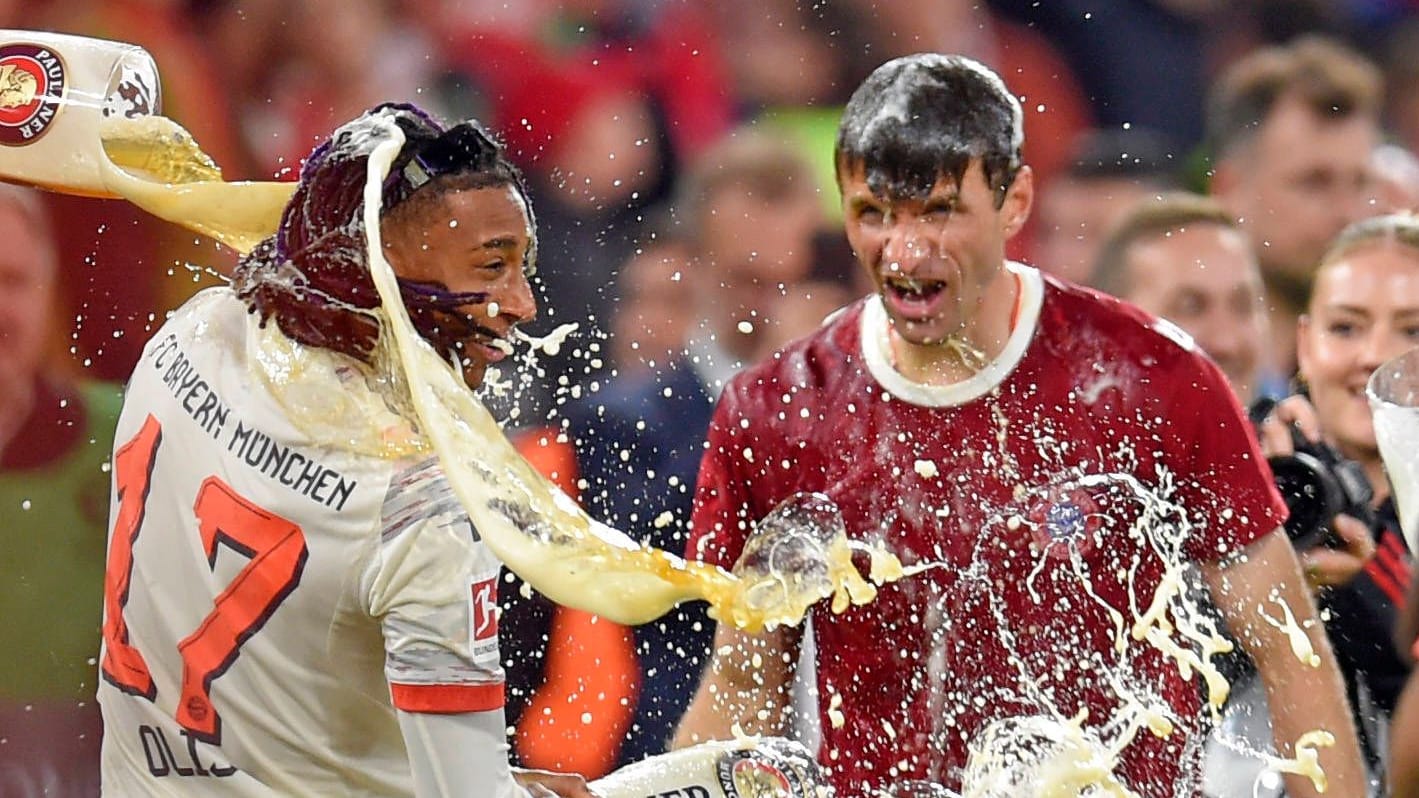 Michael Olise (links) und Thomas Müller bekommen eine Bierdusche: Das kühle Nass gehört zu den Ritualen bei einer Bayern-Meisterfeier.